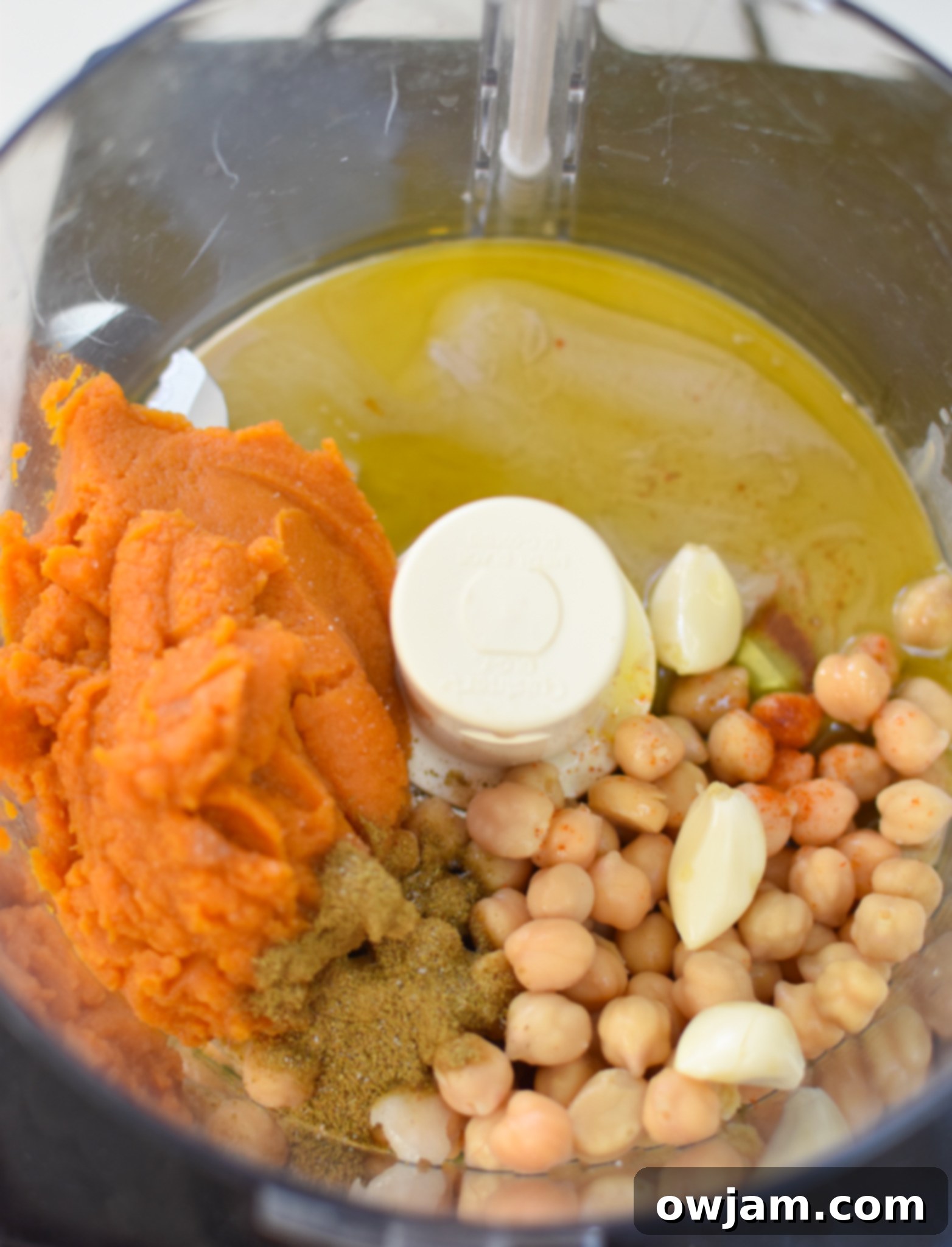 Velvet Pumpkin Dip 5 Ingredients for creamy pumpkin hummus being added to a food processor bowl, including chickpeas and pumpkin puree.
