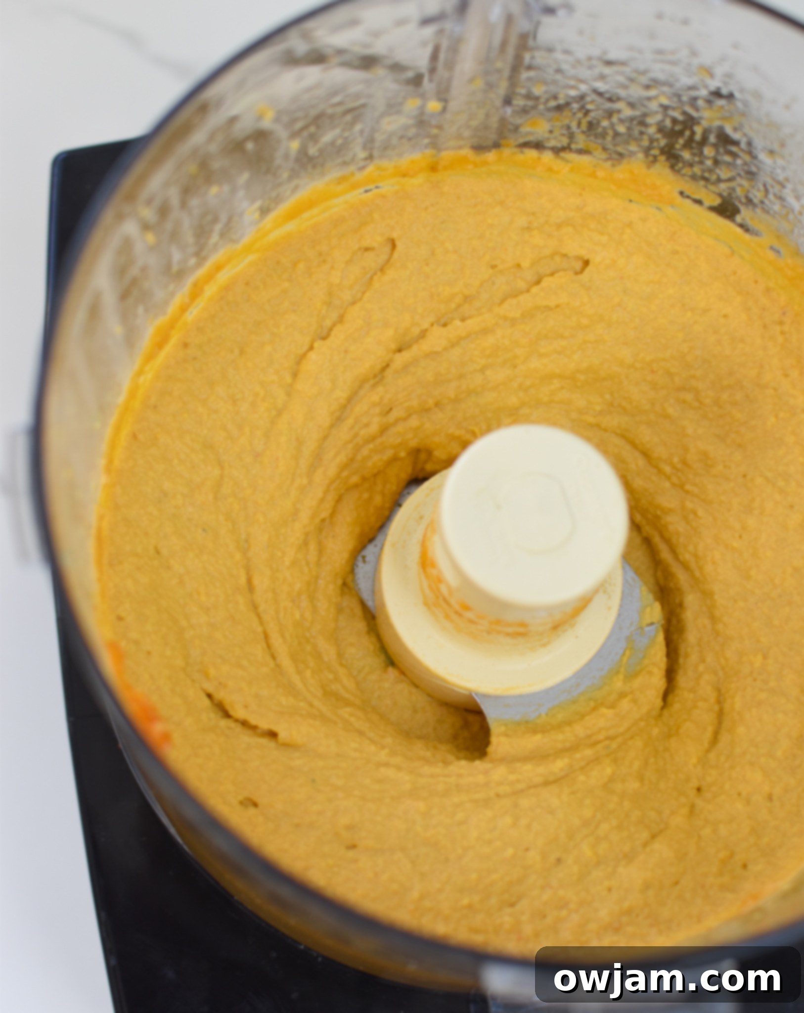 Velvet Pumpkin Dip 6 Close-up of creamy pumpkin hummus blending smoothly inside a food processor bowl, ready to be served as a fall appetizer.