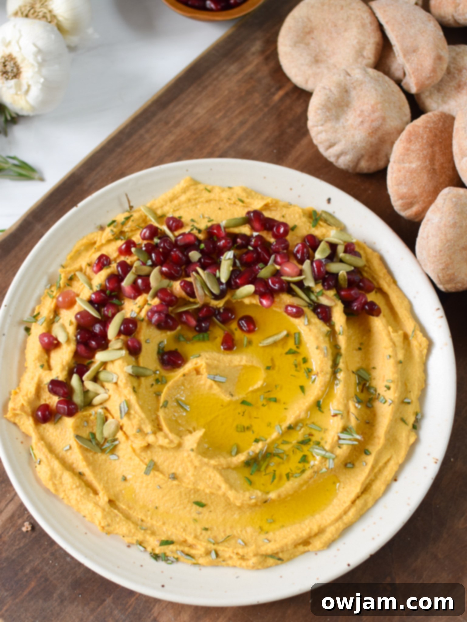 Velvet Pumpkin Dip 7 Creamy Pumpkin Hummus served with warm pita bread wedges, garnished with pumpkin seeds and fresh herbs.