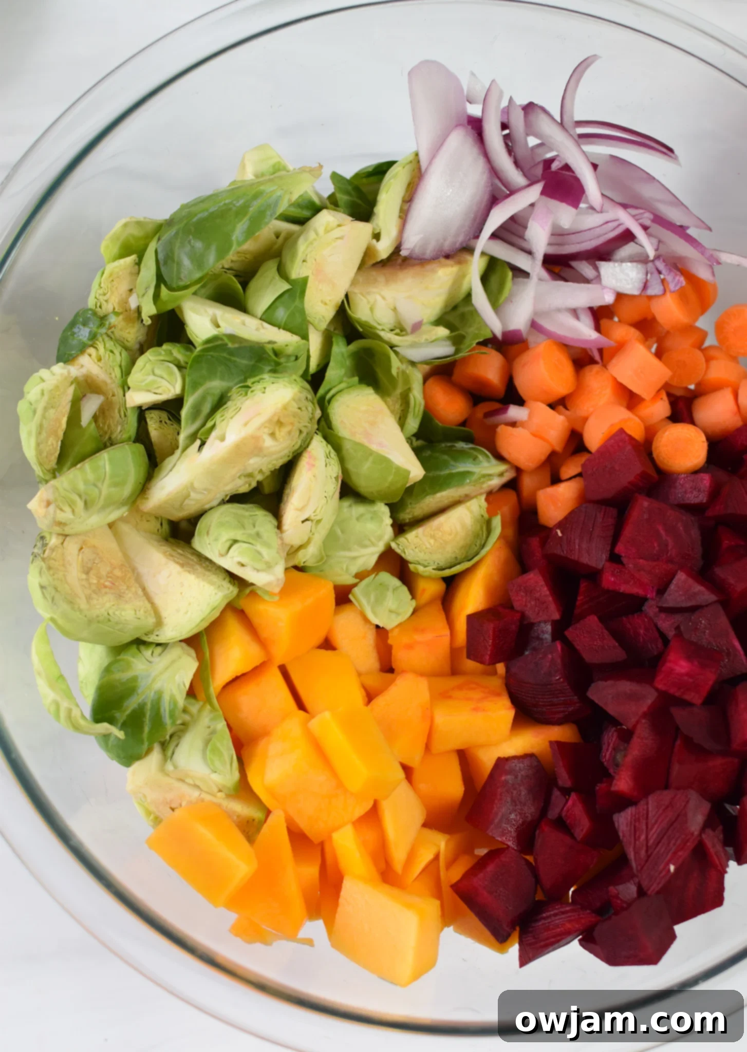 Autumn Bounty Bowl 6 Close-up of diced butternut squash, beets, Brussels sprouts, carrots, and red onion mixed with olive oil, salt, and pepper in a large bowl, ready for roasting.