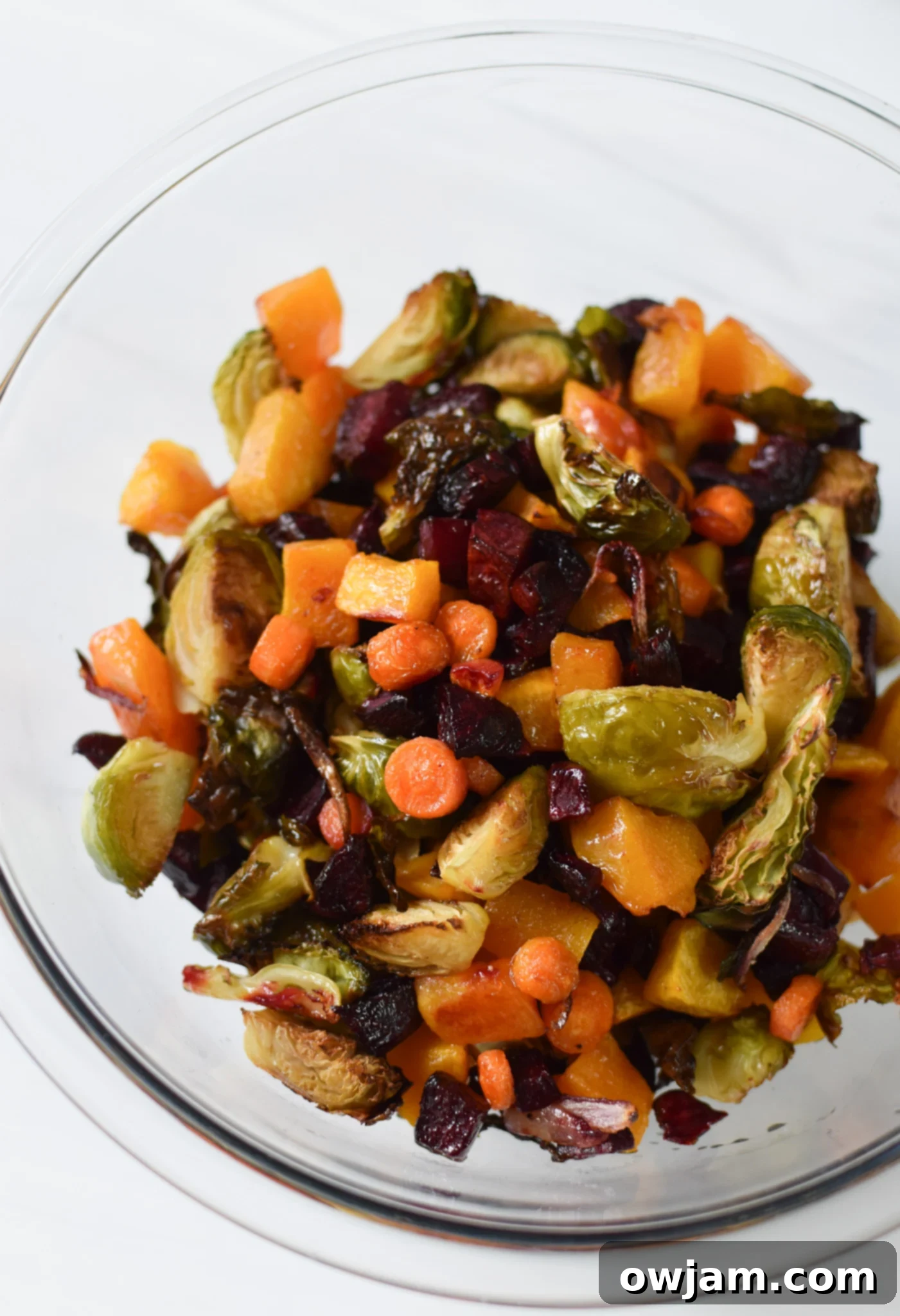 Autumn Bounty Bowl 7 Roasted butternut squash, beets, Brussels sprouts, carrots, and red onion spread on a parchment-lined baking sheet, glistening and slightly caramelized after roasting.