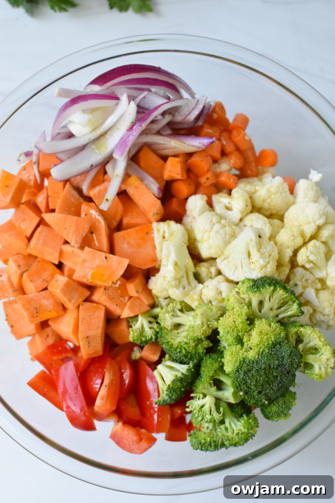 Mixed sweet potatoes and vegetables in a bowl, seasoned and ready for roasting.