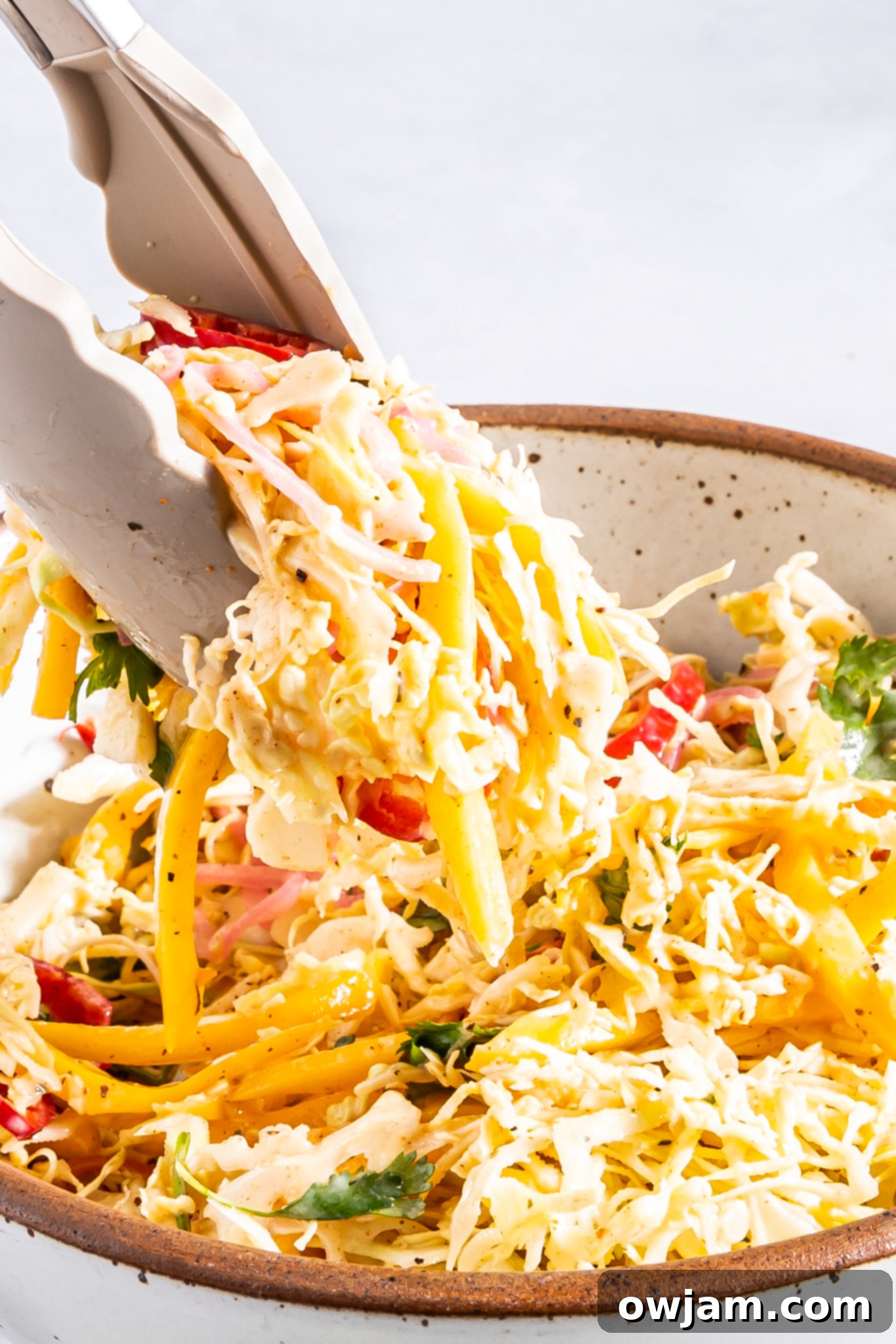 Easy Caribbean Coleslaw Recipe being tossed with tongs in a large bowl.