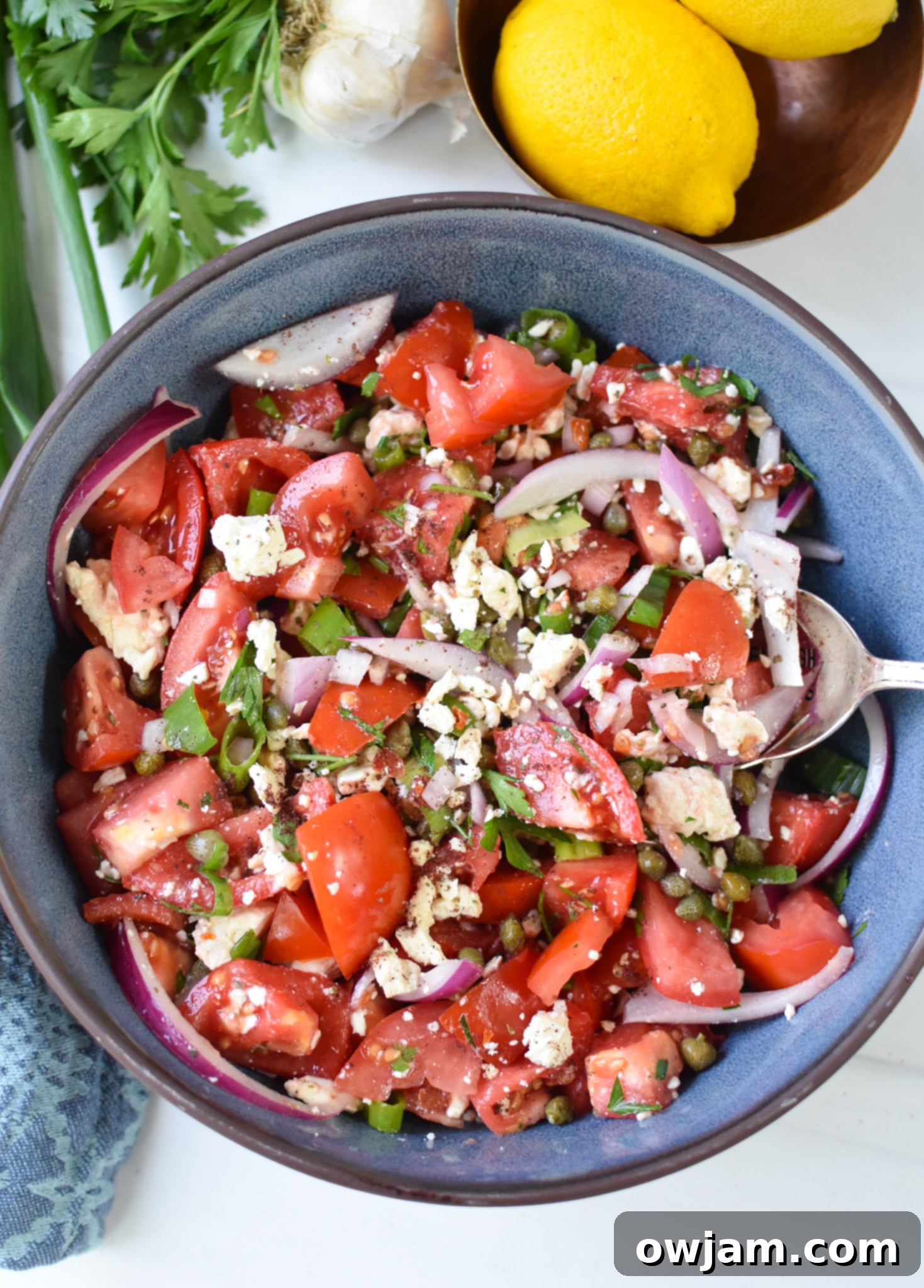 Quick and Fresh Tomato Salad 6 Easy Tomato Salad in a blue bowl with a serving spoon, ready to eat.
