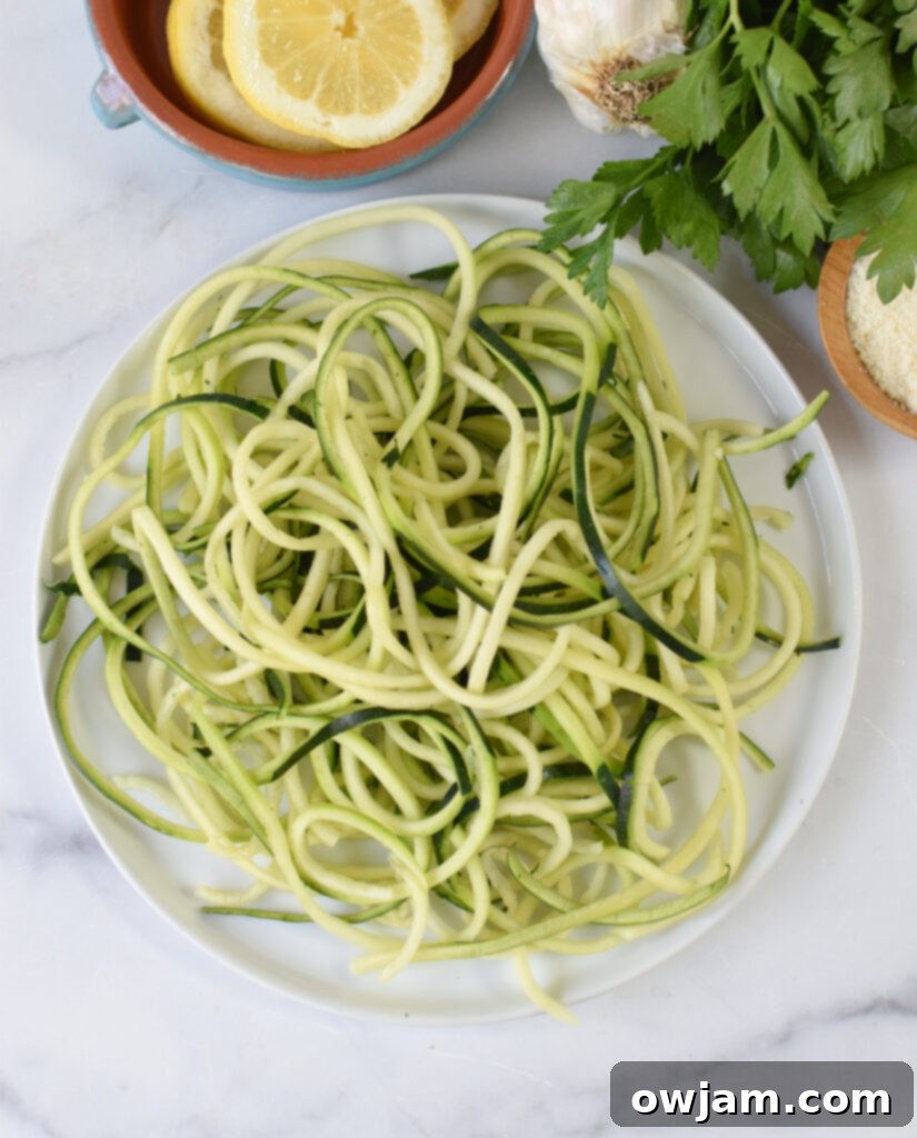 Close-up of fresh zucchini noodles, ready to be added to a dish, highlighting their vibrant green color and delicate spiral shape.