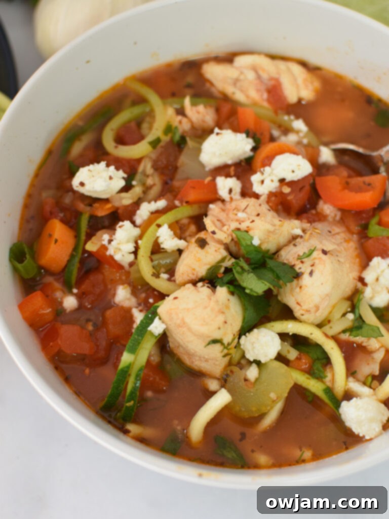 A steaming bowl of Mediterranean Fish Soup, garnished with fresh herbs and a lime wedge, placed on a white surface.