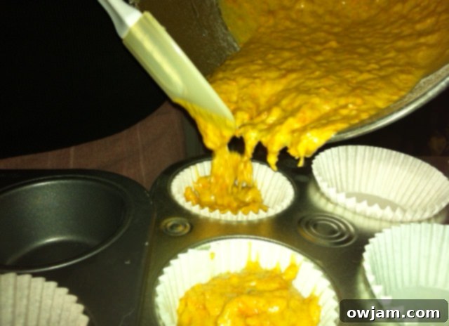 Scooping carrot cupcake batter into muffin liners with a spatula for even distribution