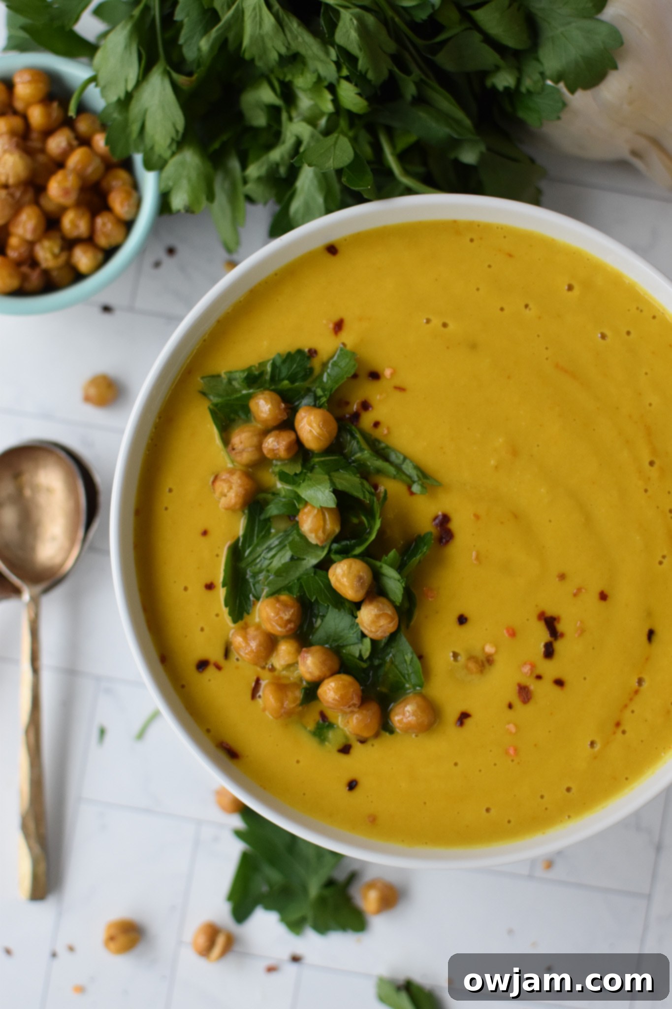 Velvety Roasted Cauliflower Soup 2 A bowl of creamy cauliflower soup, garnished with crispy chickpeas, fresh parsley, and a sprinkle of red pepper flakes.