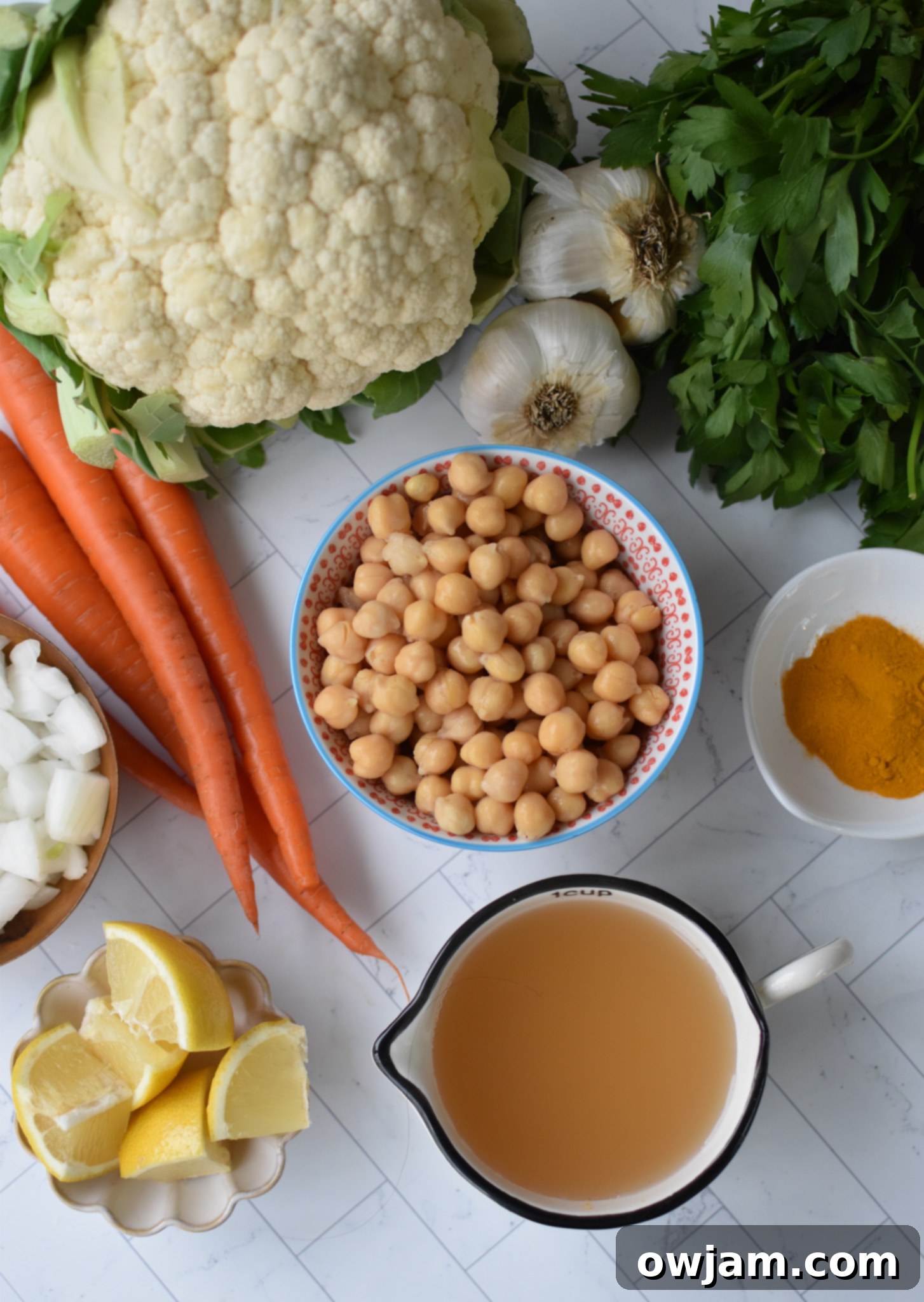 Velvety Roasted Cauliflower Soup 3 A selection of fresh ingredients for creamy cauliflower soup including cauliflower florets, garlic, ginger, onion, carrots, turmeric, paprika, chickpeas, and lemon.