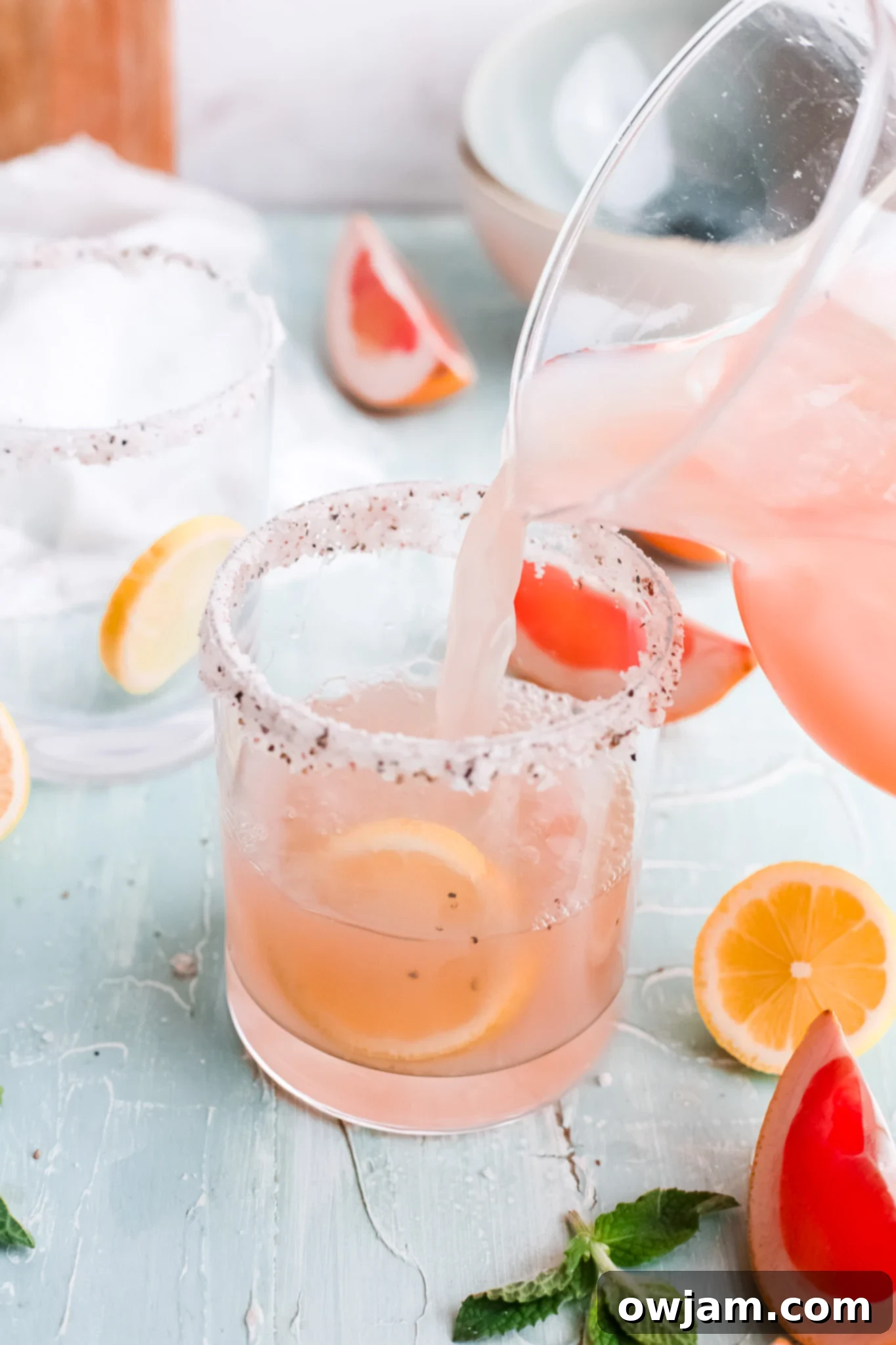 Tangy Grapefruit Paloma 6 Grapefruit Paloma Cocktail being poured from a pitcher into a salt-rimmed glass.