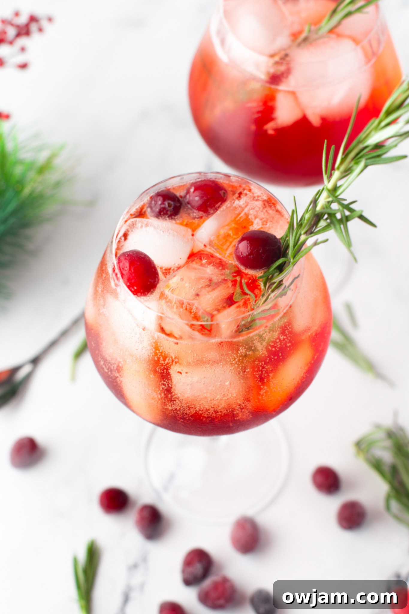 Two glasses of Cranberry Aperol Spritz garnished with fresh cranberries and rosemary.