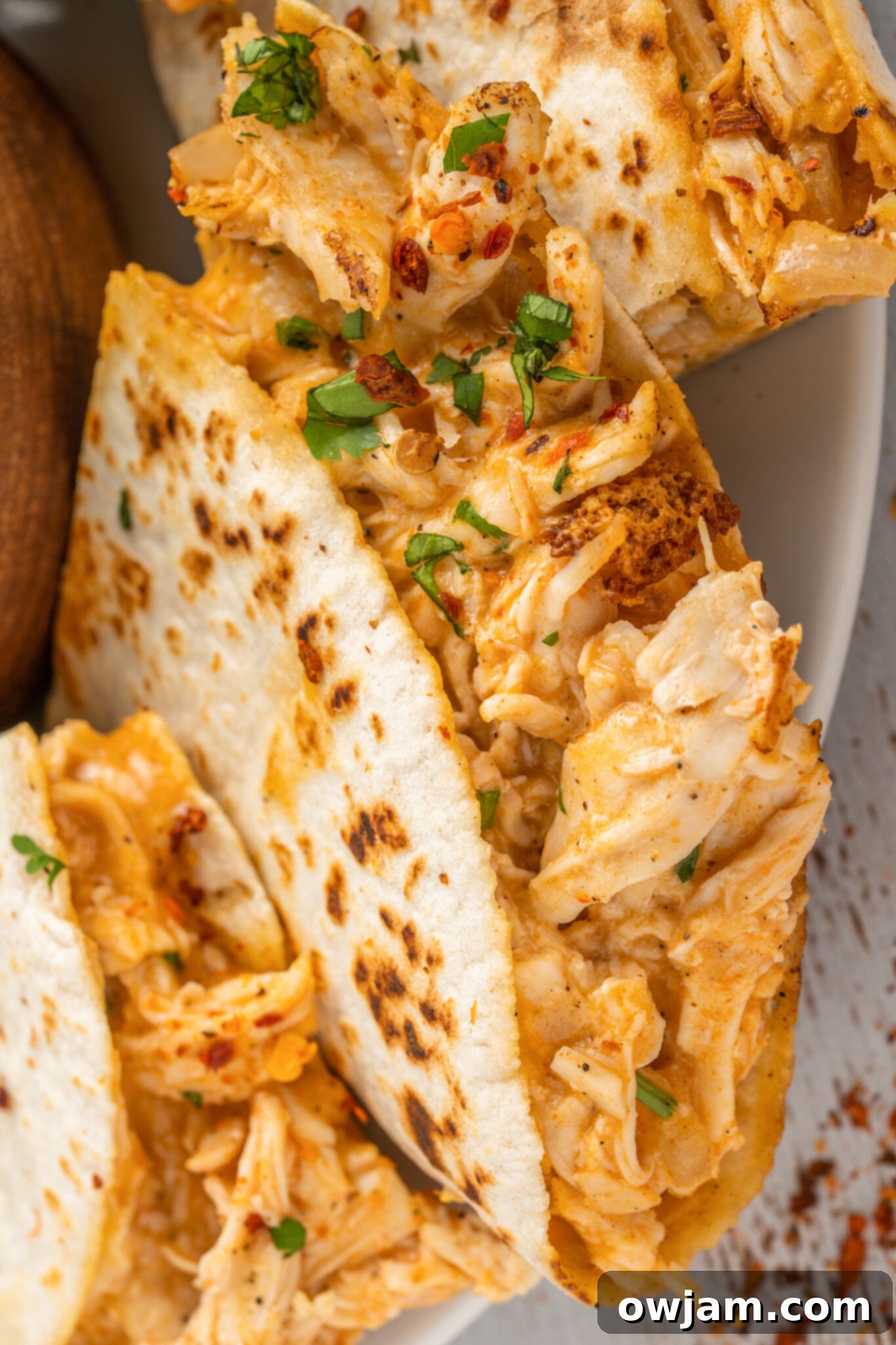 Spicy Cheesy Buffalo Chicken Quesadillas 4 A buffalo chicken quesadilla, cut in half, garnished with fresh cilantro on a white plate.