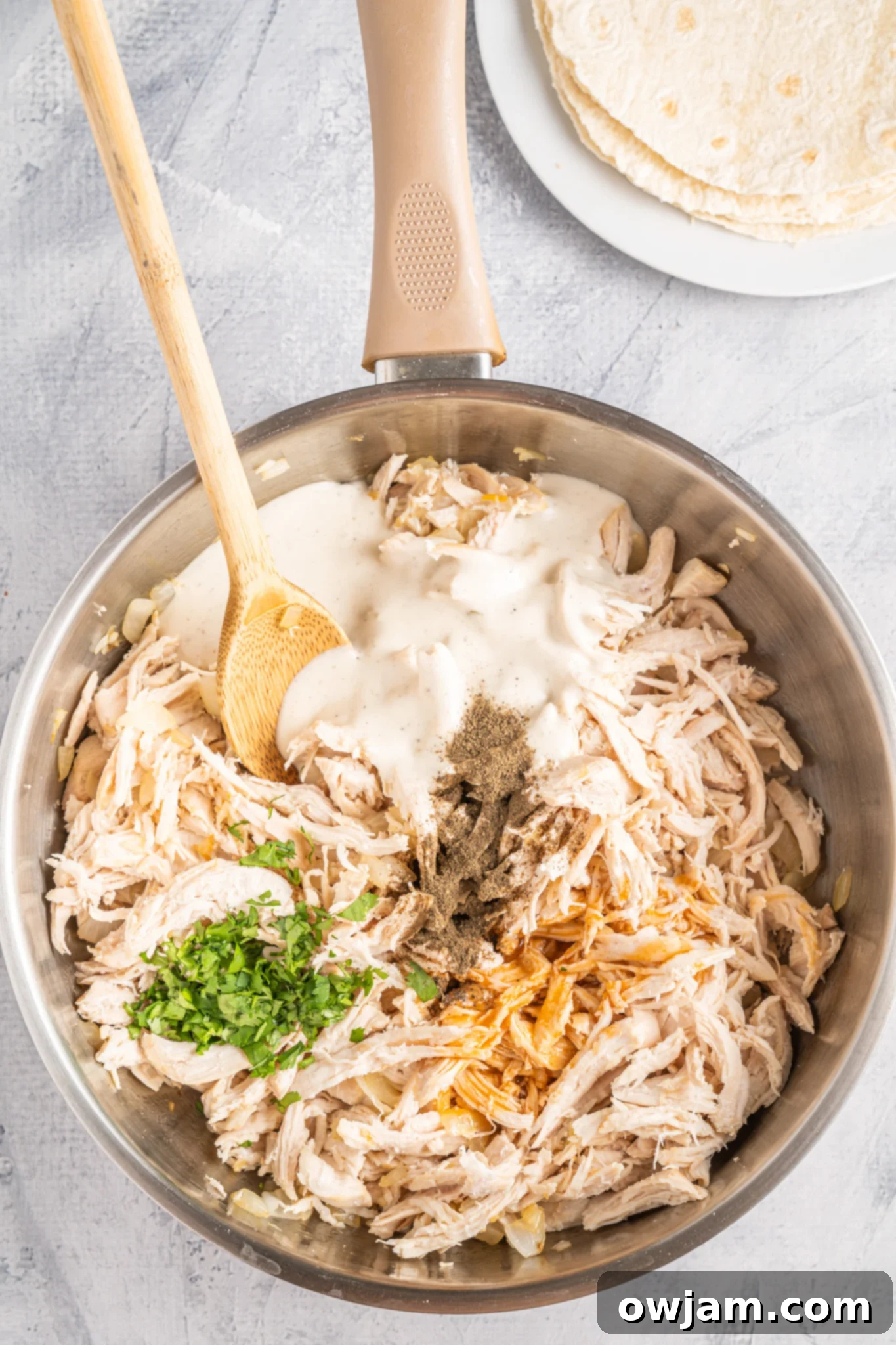 Spicy Cheesy Buffalo Chicken Quesadillas 6 Shredded chicken being added to the sautéed onion and garlic in a skillet, ready to be mixed with buffalo sauce.