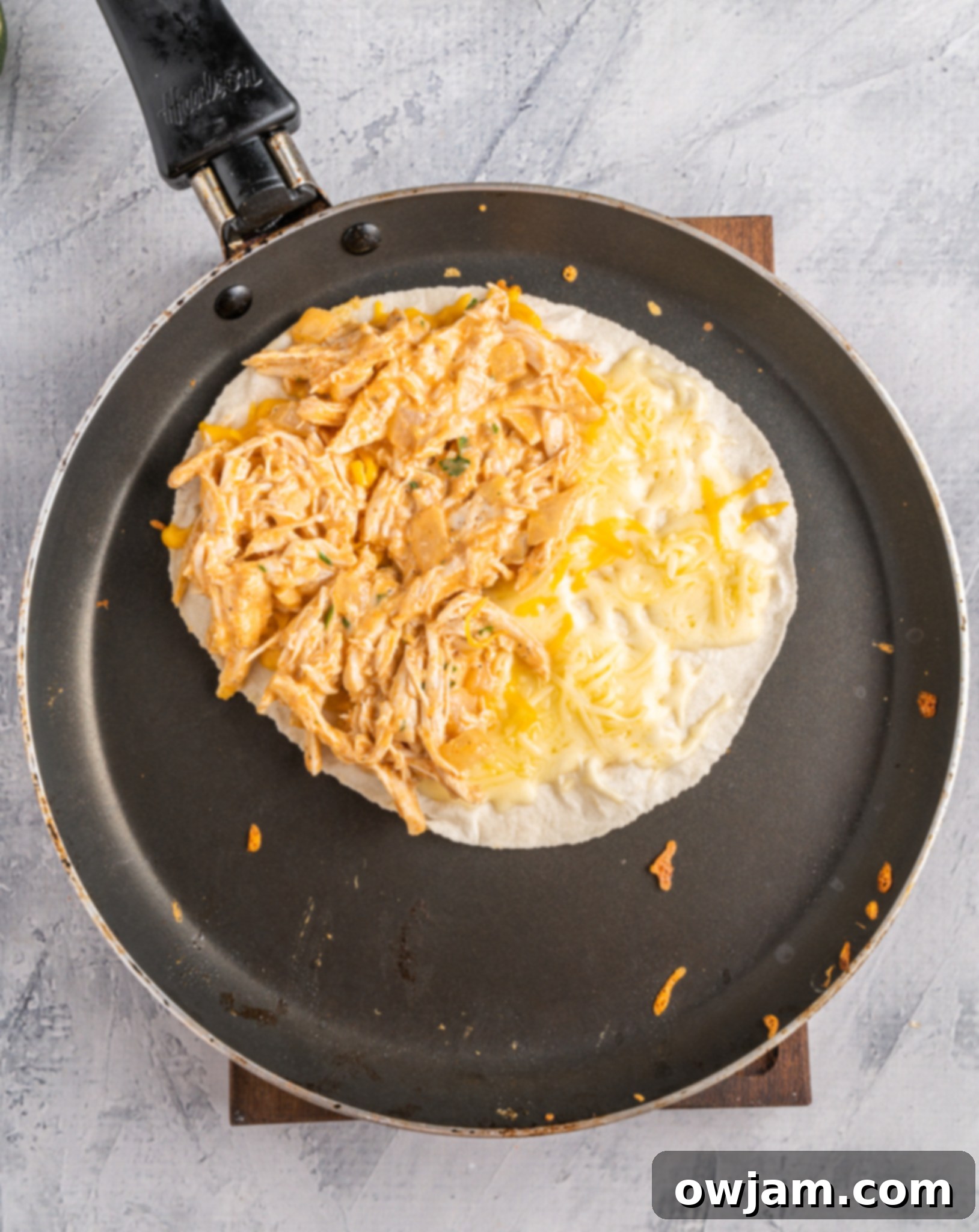 Spicy Cheesy Buffalo Chicken Quesadillas 8 A tortilla in a skillet with melted cheese and buffalo chicken filling on one half, ready to be folded.