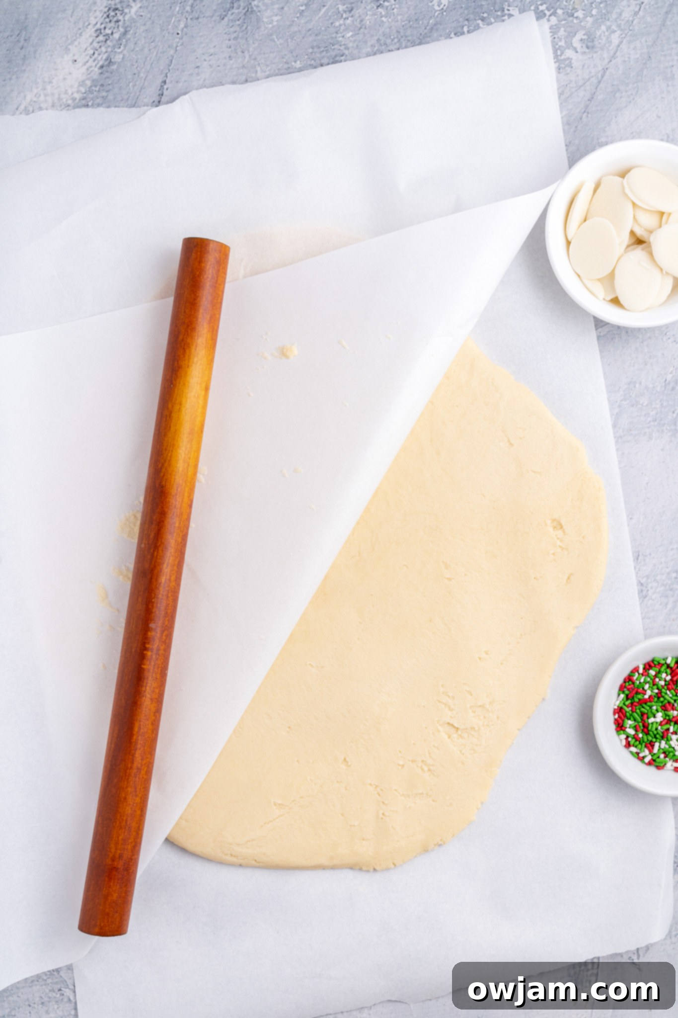 Christmas Shortbread Cookies dough being rolled between two sheets of parchment paper with a rolling pin.