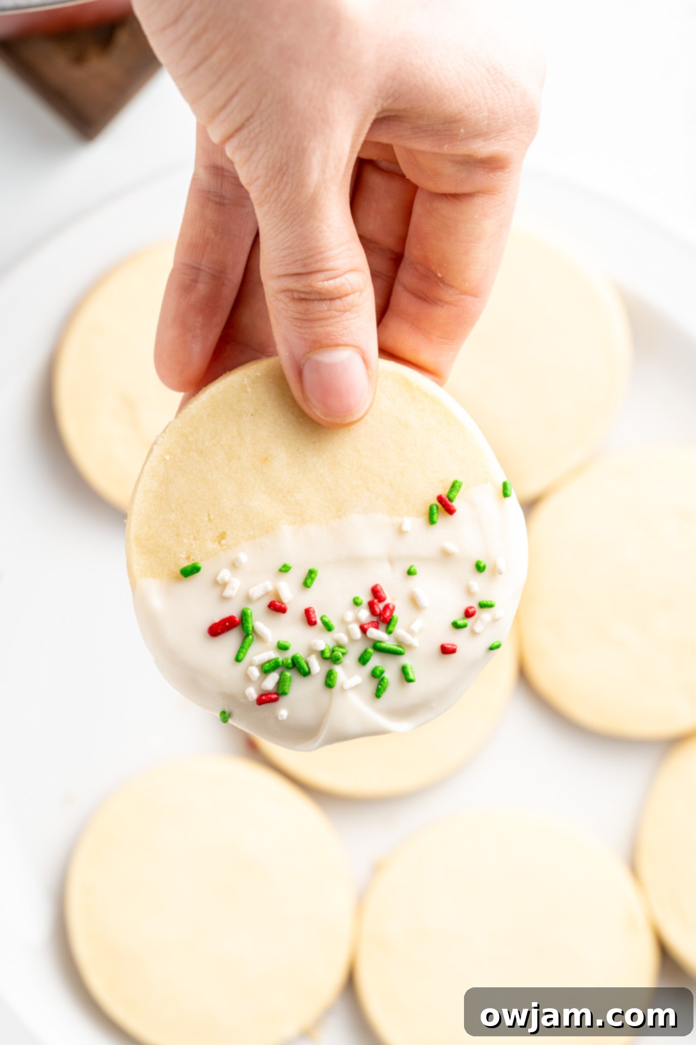 A Christmas Shortbread Cookie being dipped in melted white chocolate, ready for sprinkles.