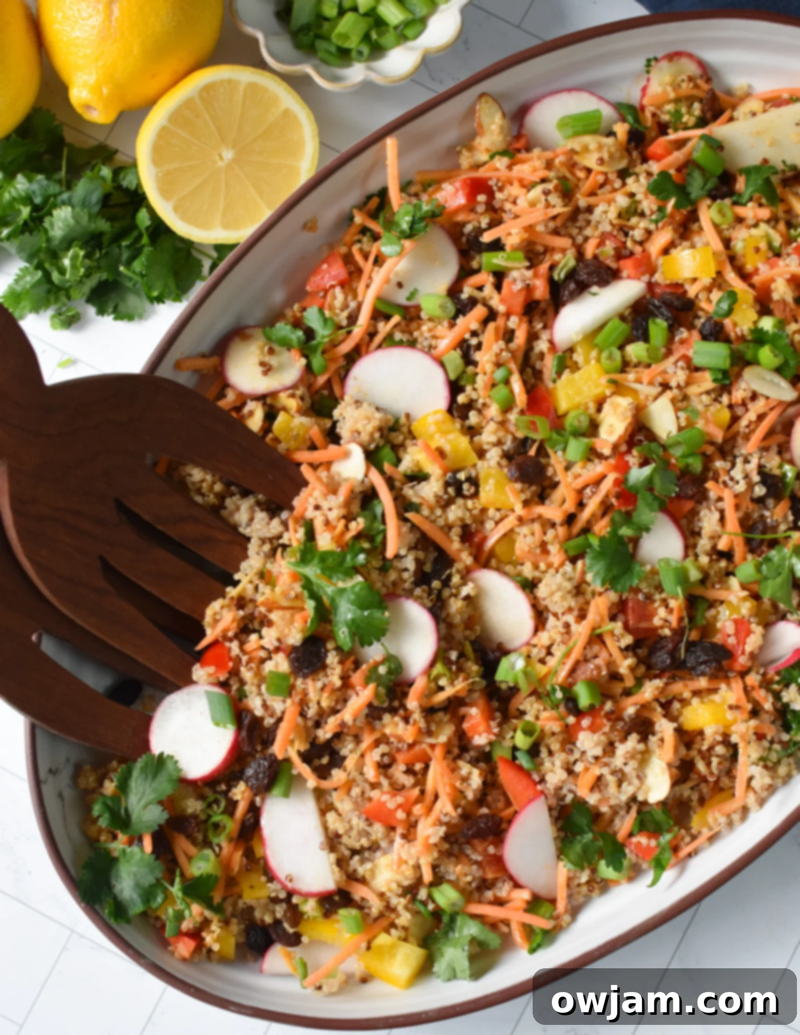 A vibrant Curried Quinoa Salad presented in a large bowl with wooden serving tongs, showcasing colorful vegetables and fluffy quinoa.