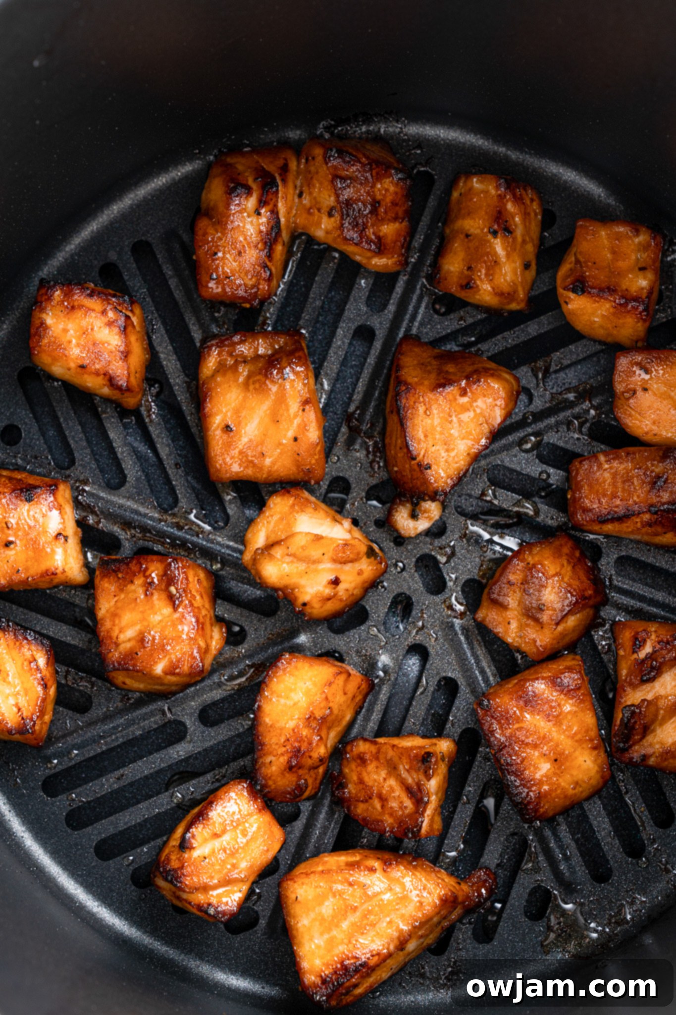 Crispy Teriyaki Air Fryer Salmon Bites 6 Chunks of glazed salmon are evenly spaced and cooked inside an air fryer basket. The pieces are golden brown with a slight char, indicating they are cooked and ready to eat.