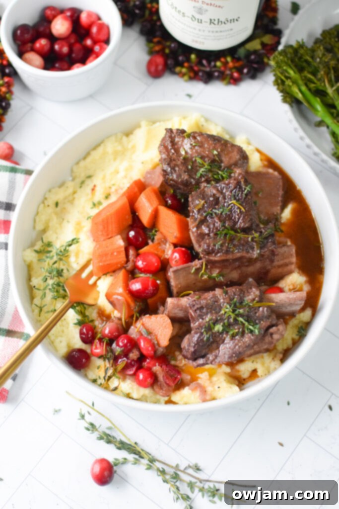 Festive Cranberry Braised Short Ribs 9 Plated Cranberry Braised Short Ribs Recipe with a fork showing tender meat, garnished with fresh herbs.