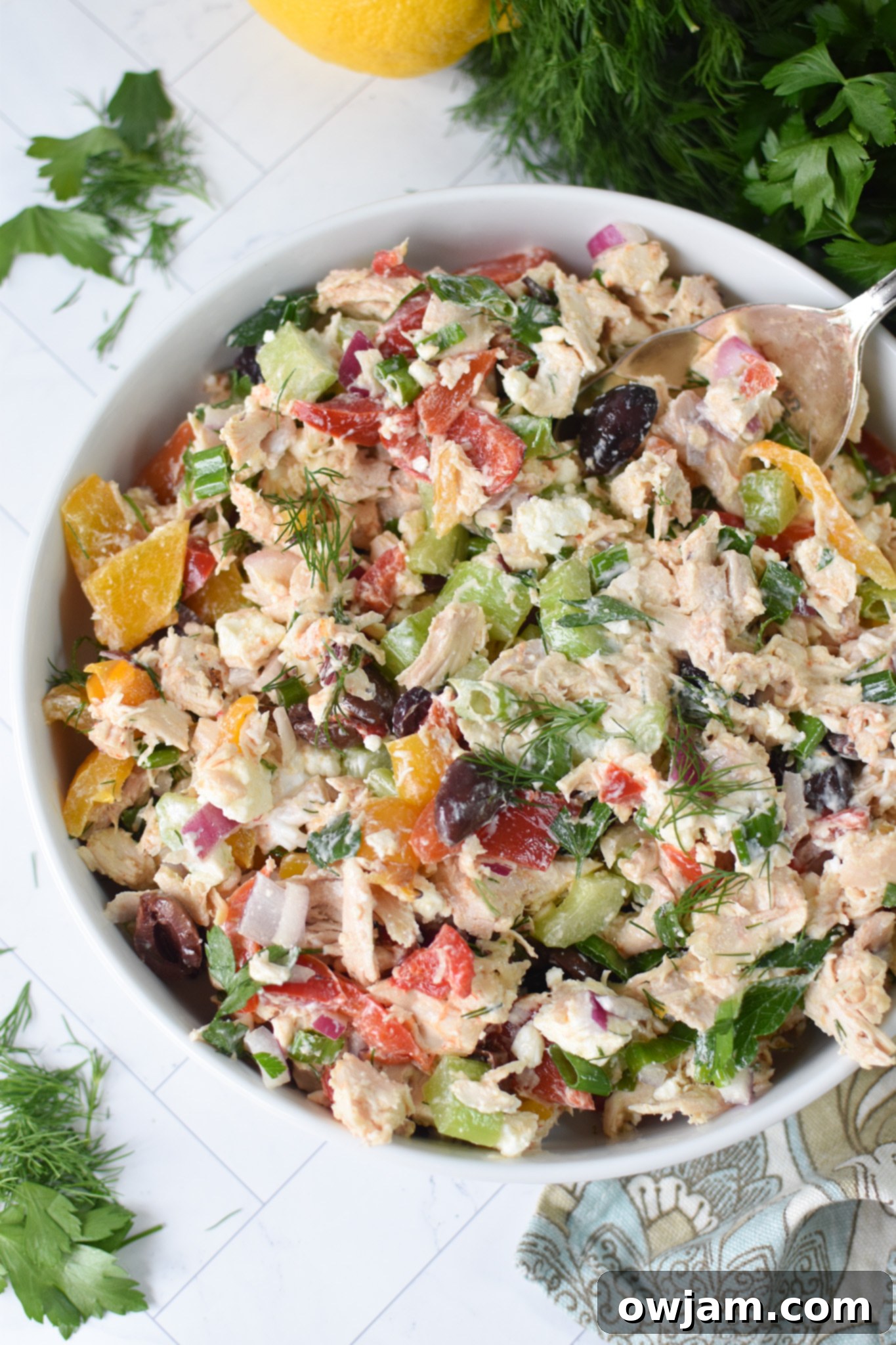 Healthy Mediterranean Chicken Salad in a white bowl, garnished with fresh herbs and a lemon wedge.