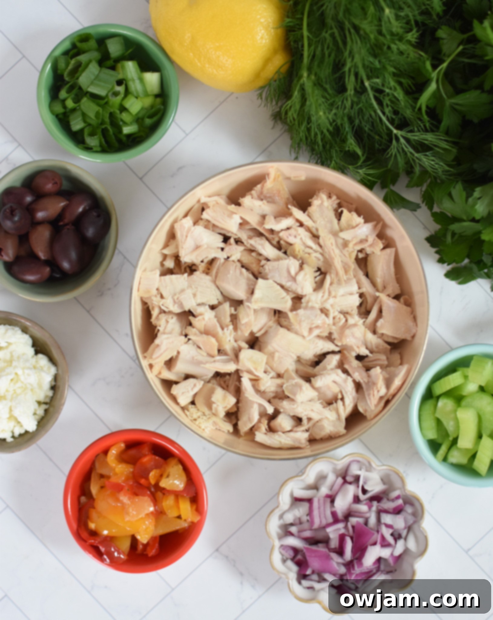 Fresh, colorful ingredients for Healthy Mediterranean Chicken Salad, including feta, olives, and roasted red peppers, laid out for preparation.