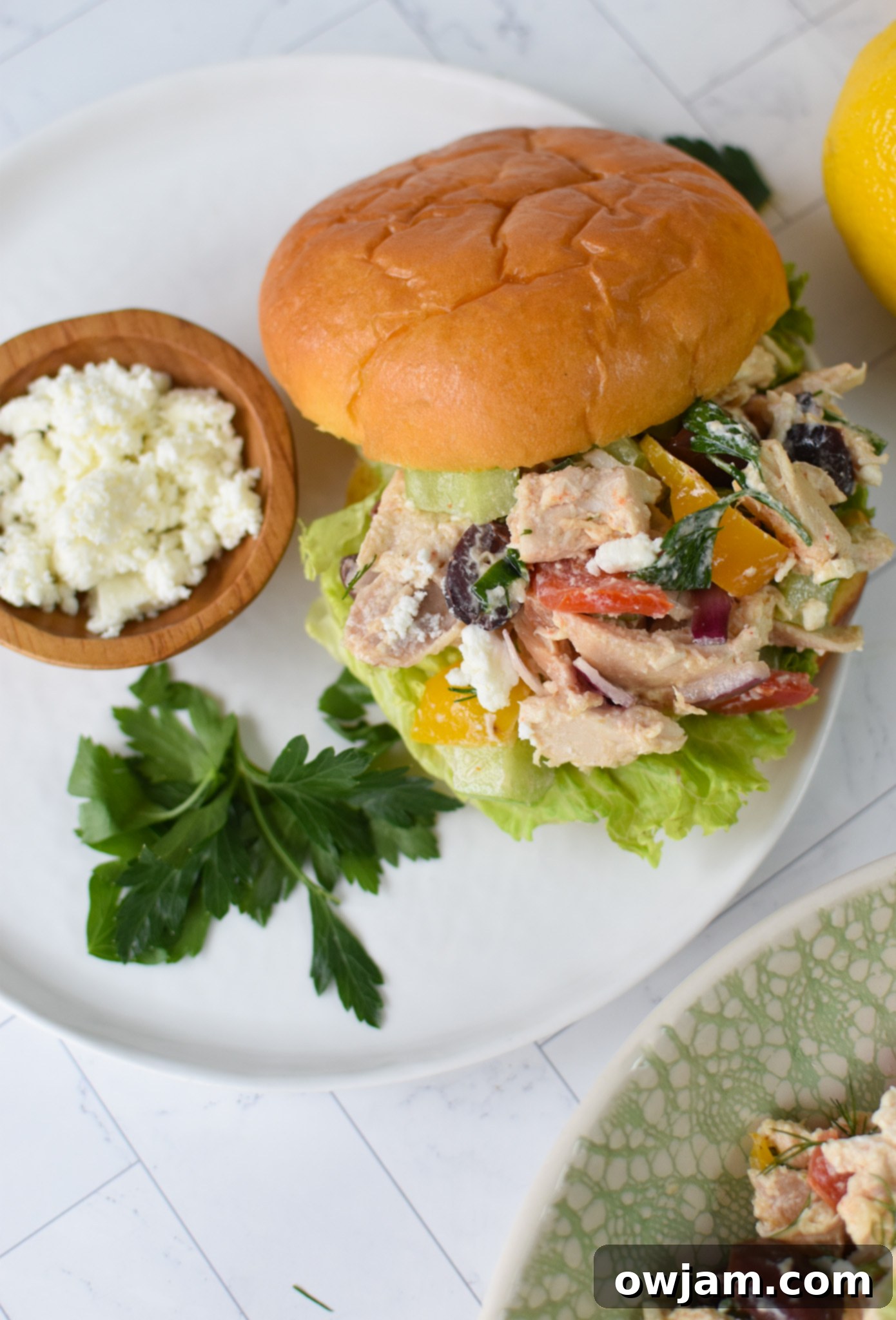 Healthy Mediterranean Chicken Salad served on a soft bun with a side salad and lemon wedge.
