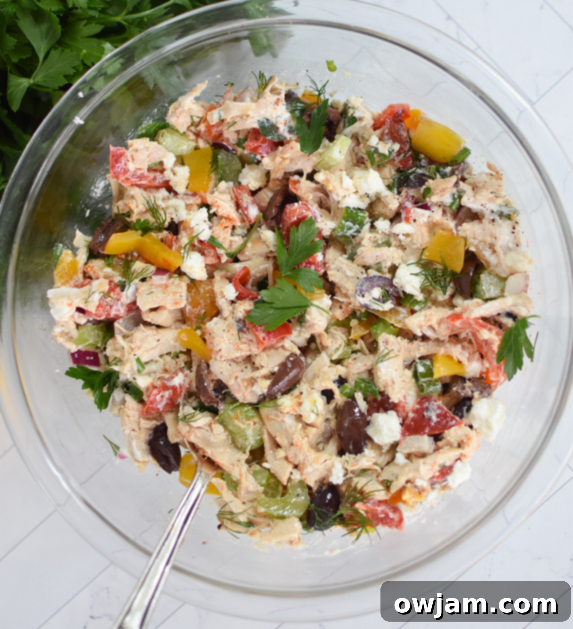 Close-up of Healthy Mediterranean Chicken Salad with dressing and herbs thoroughly mixed in a white serving bowl.