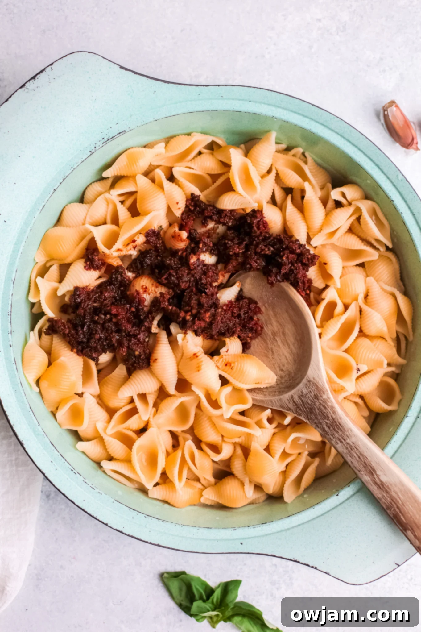 Sun-Dried Tomato Pesto being tossed with cooked pasta in a large pot, showing the sauce coating the pasta strands.
