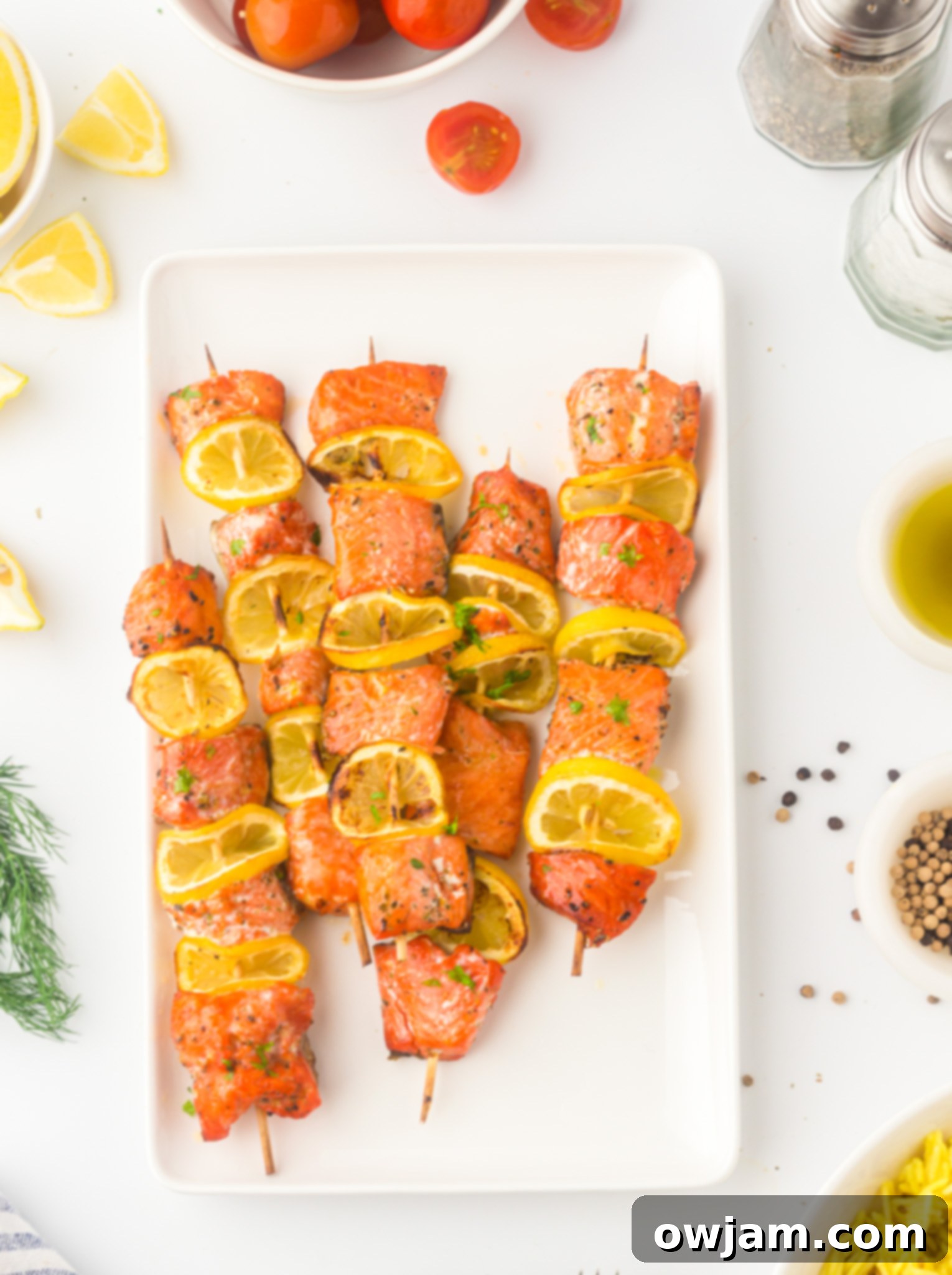 Zesty Lemon Salmon Skewers 2 Easy Lemon Salmon Kabobs on a white platter, garnished with fresh lemon slices and herbs.