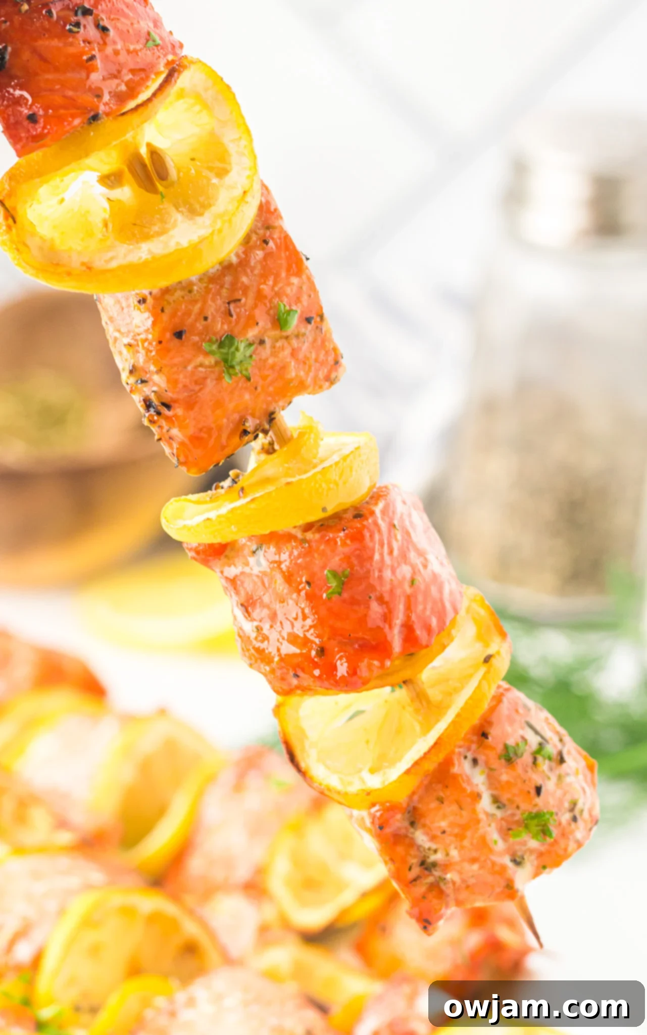 Zesty Lemon Salmon Skewers 3 Easy Lemon Salmon Kabobs on a skewer with lemon slices and fresh herbs.