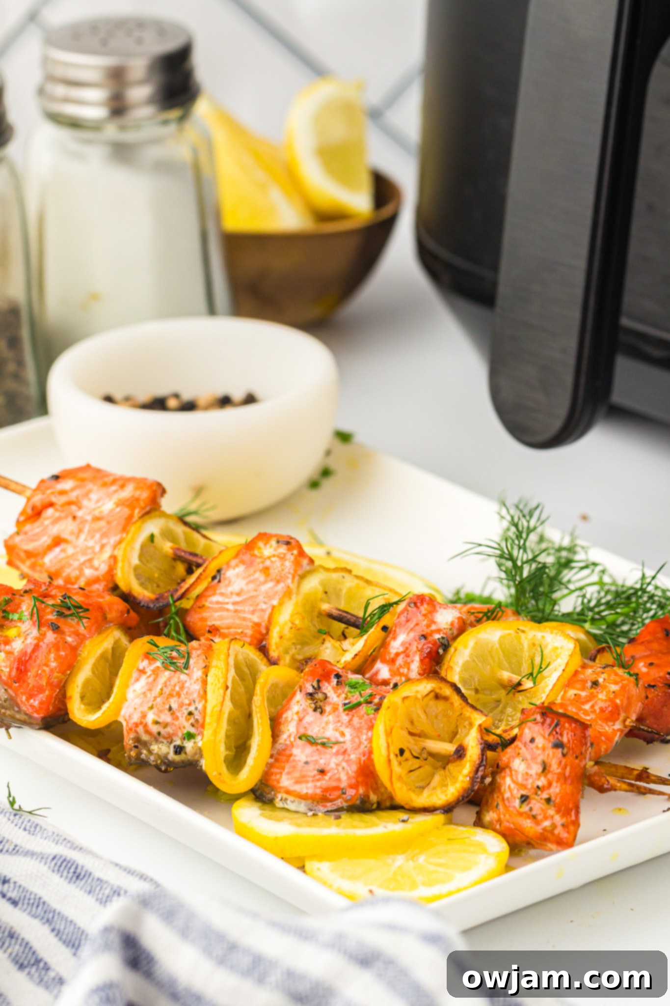 Zesty Lemon Salmon Skewers 5 Cooked Easy Lemon Salmon Kabobs on a white plate, with an air fryer visible in the soft background.