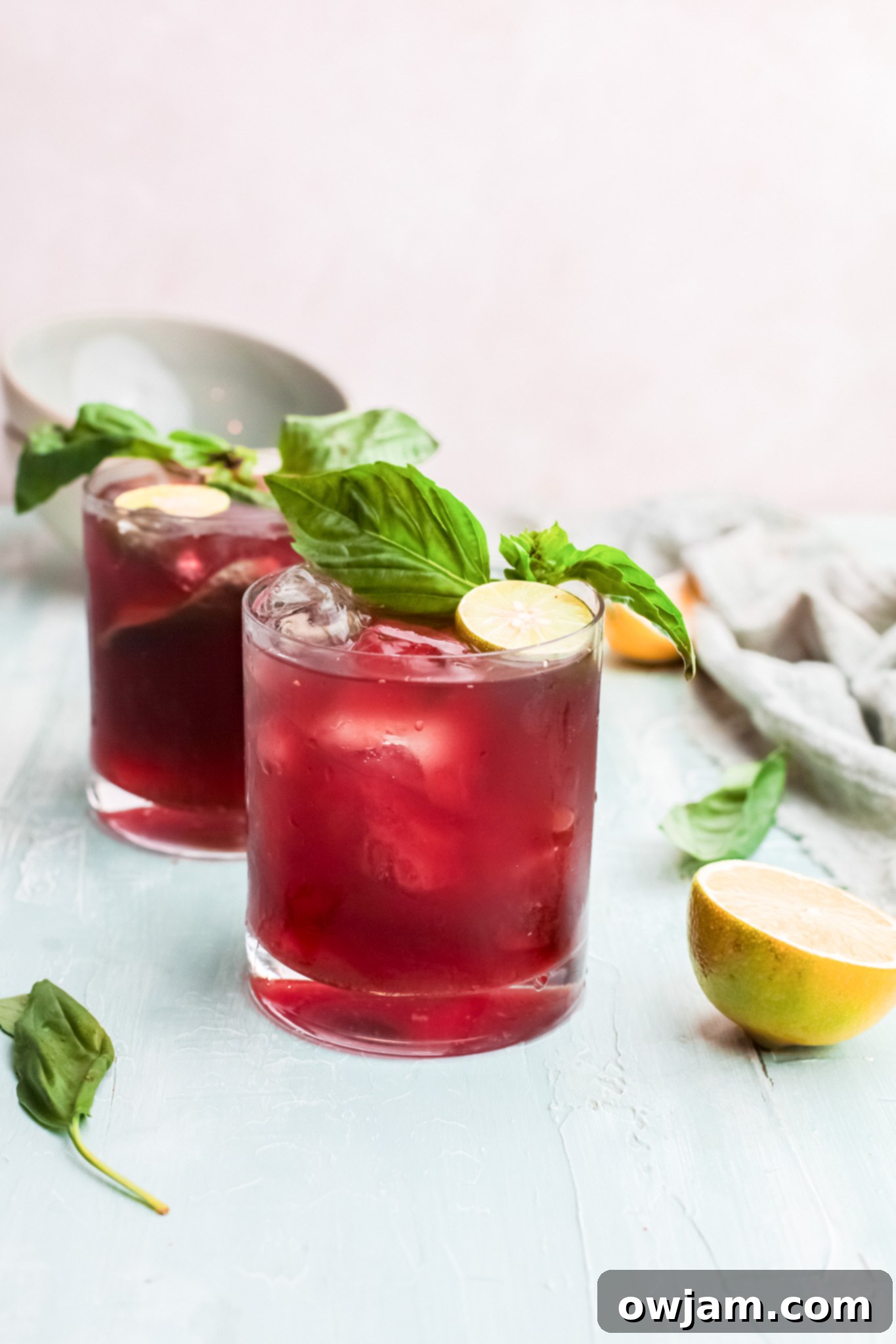 Two glasses of Vodka Cherry Limeade, garnished with lime slices, on a light surface.