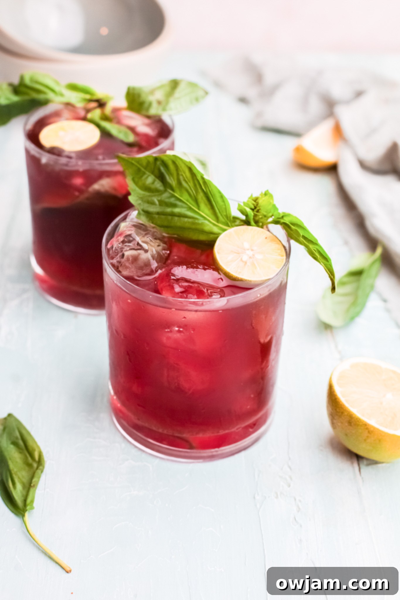 Two vibrant Vodka Cherry Limeade cocktails garnished with lime, basil, and mint.