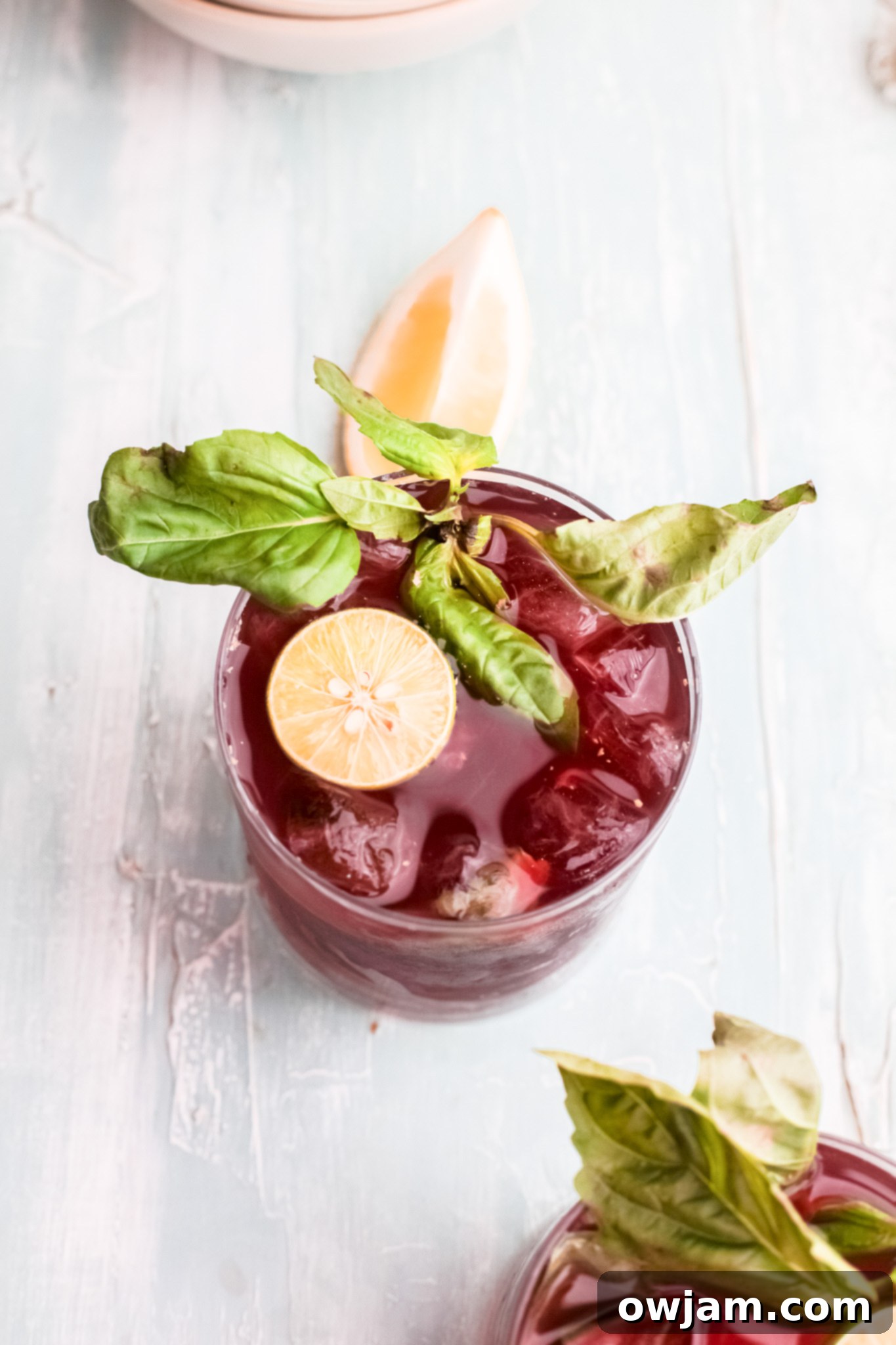 A single glass of Vodka Cherry Limeade, garnished with lime and basil, showcasing its vibrant color.