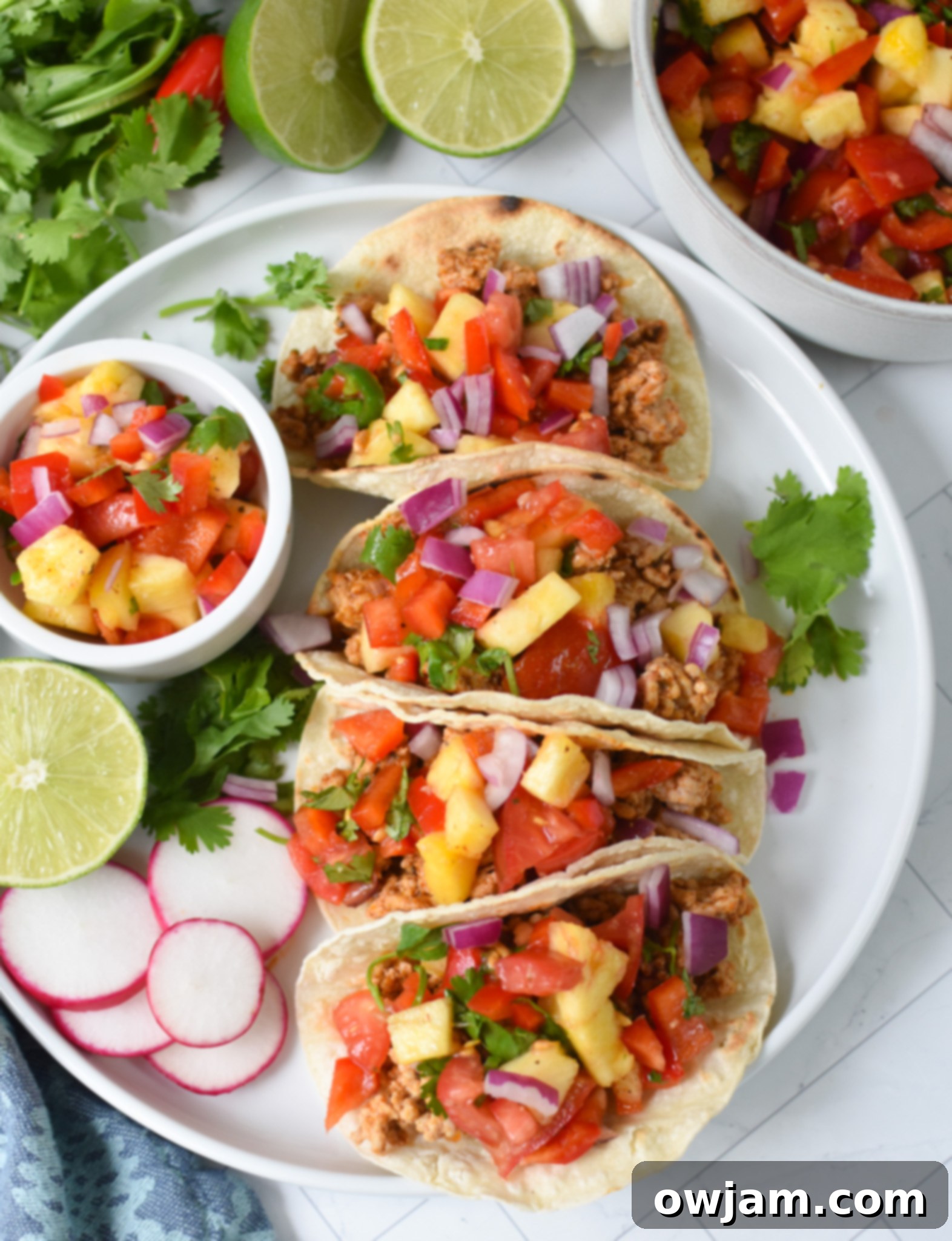 Effortless Ground Pork Tacos 2 Easy Ground Pork Tacos on white plate, topped with pineapple salsa and fresh cilantro.