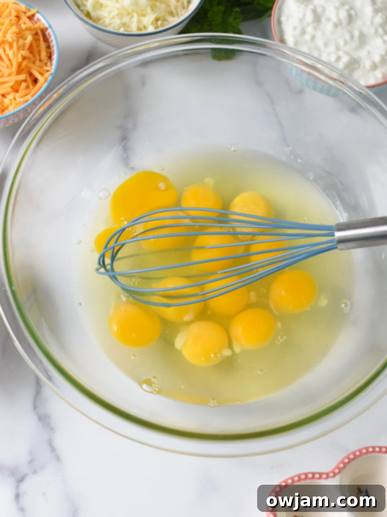 Close-up of eggs being whisked in a glass bowl for the baked eggs recipe.
