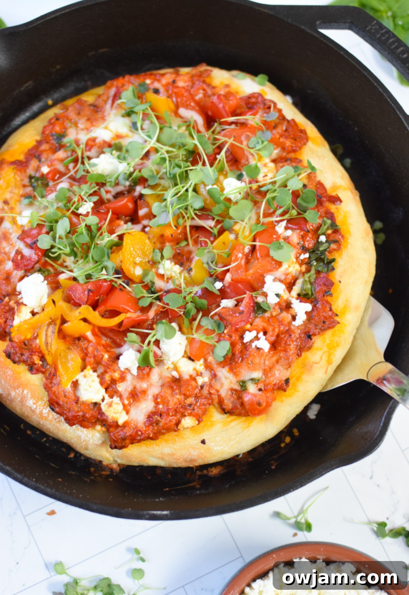 Rustic Cast Iron Mediterranean Pizza 8 A cast iron skillet pizza being lifted with a spatula, showing the perfectly cooked crust.