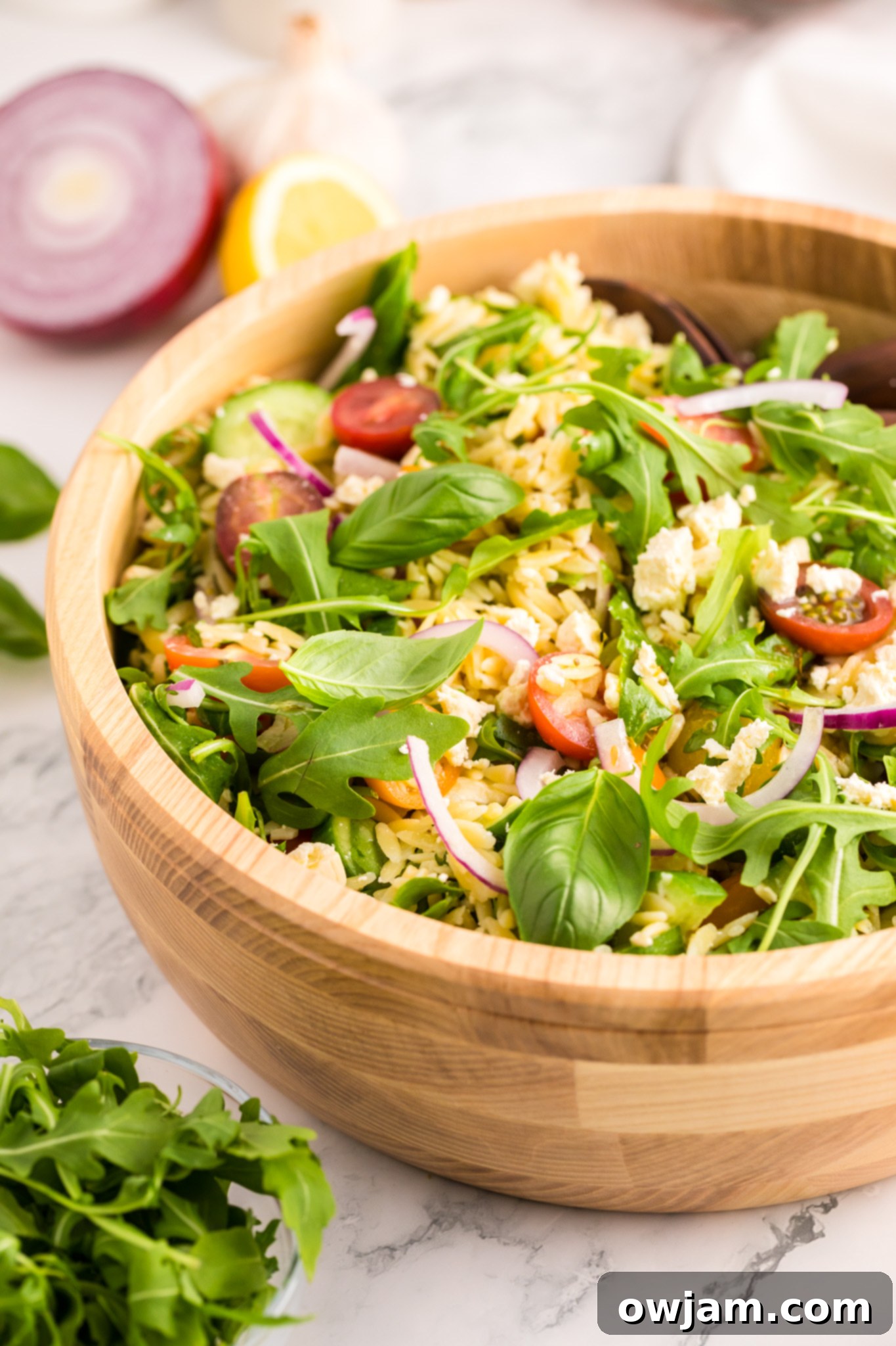 A large wooden bowl filled with the finished Arugula Orzo Salad, showcasing its inviting presentation.