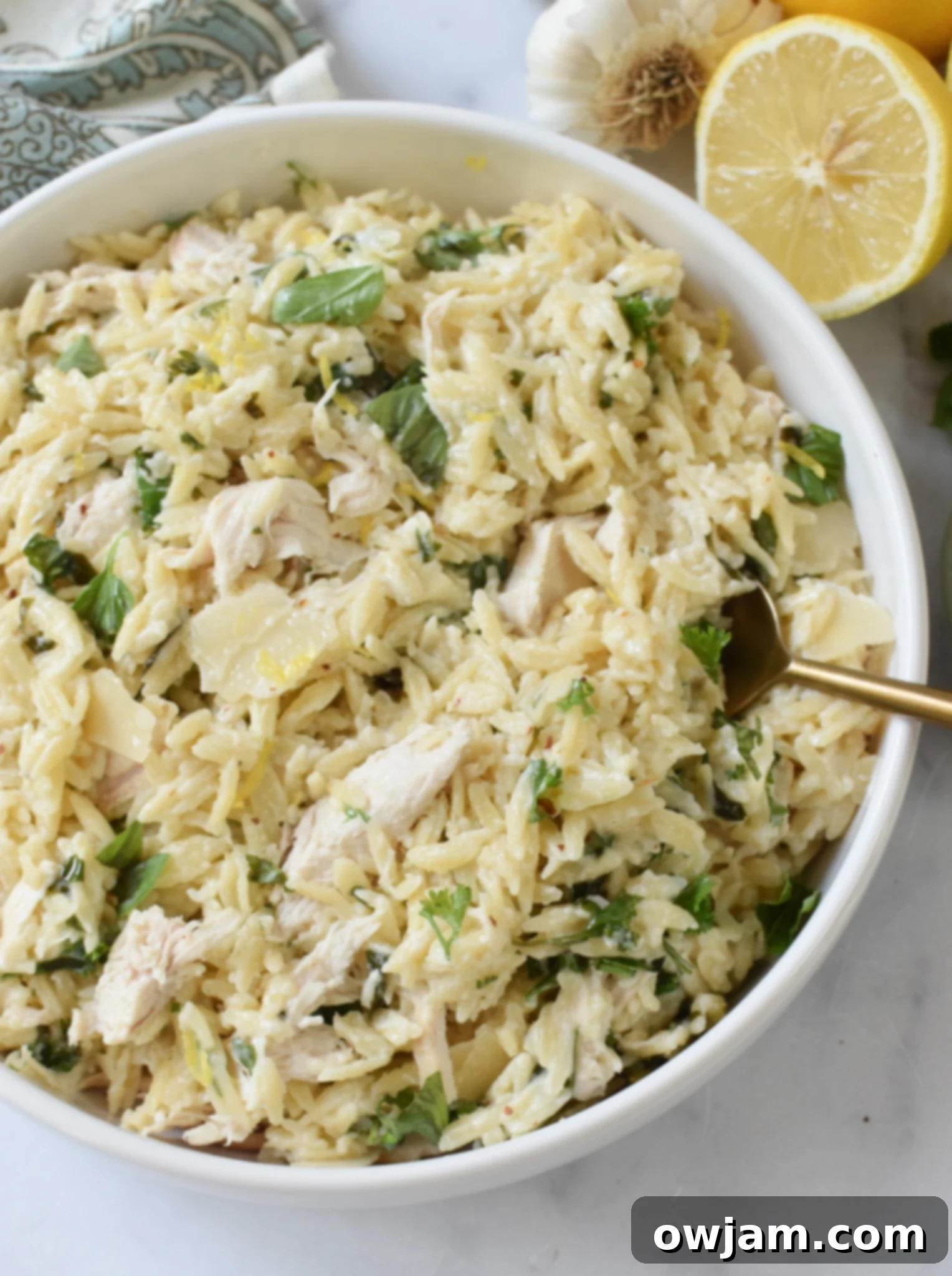 A close-up of creamy Lemon Chicken Orzo in a white bowl with a gold spoon, highlighting the rich texture and vibrant lemon.