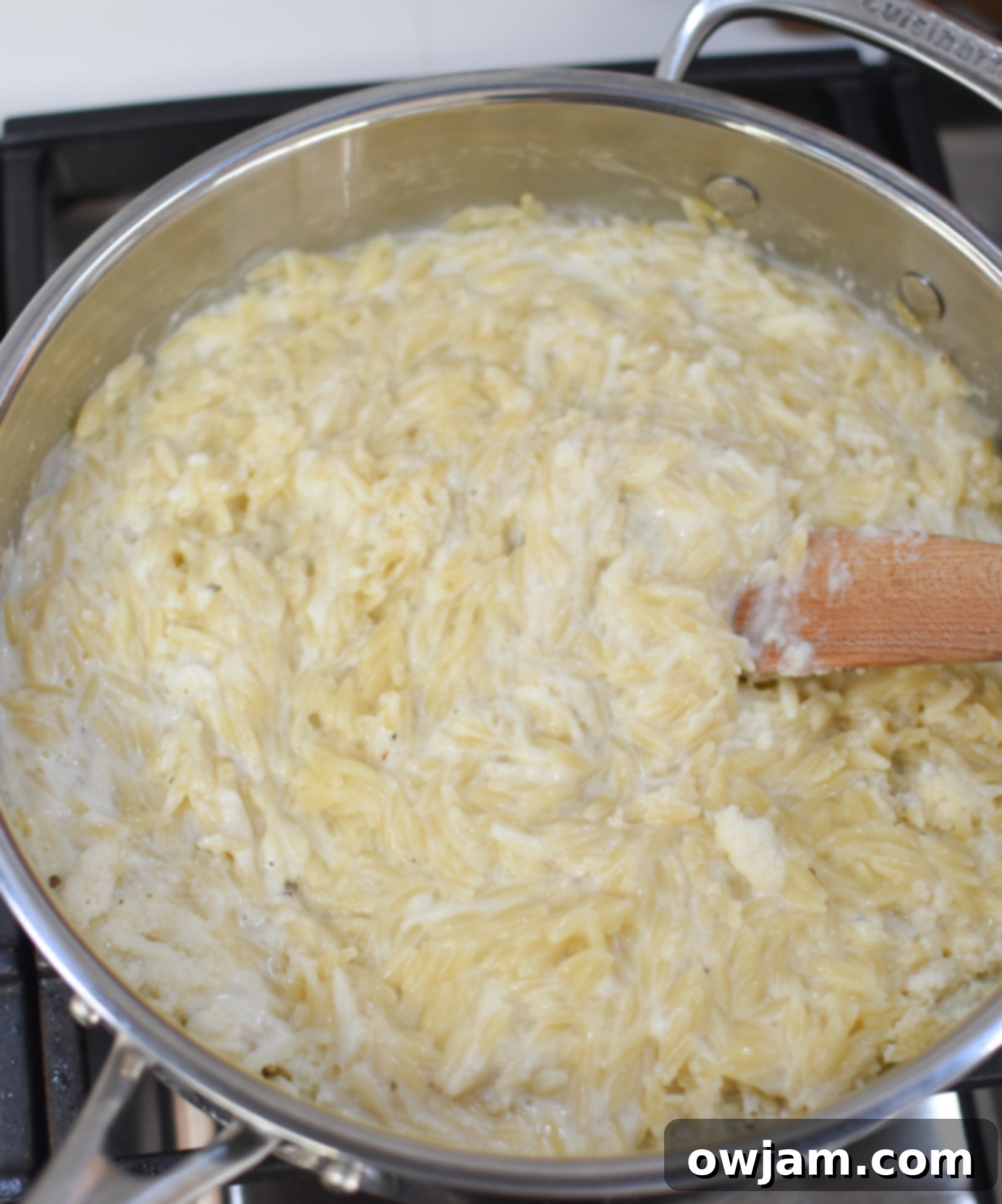 The creamy lemon sauce base for Lemon Chicken Orzo simmering in a pan with melted cheese and herbs.