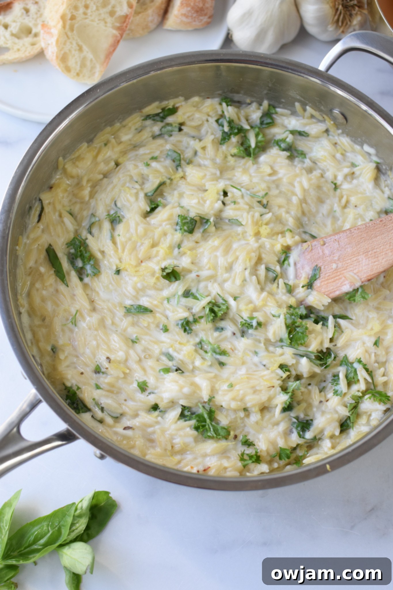 A large pot of creamy Lemon Chicken Orzo ready to be served, with a wooden serving spoon dipped into the pasta.