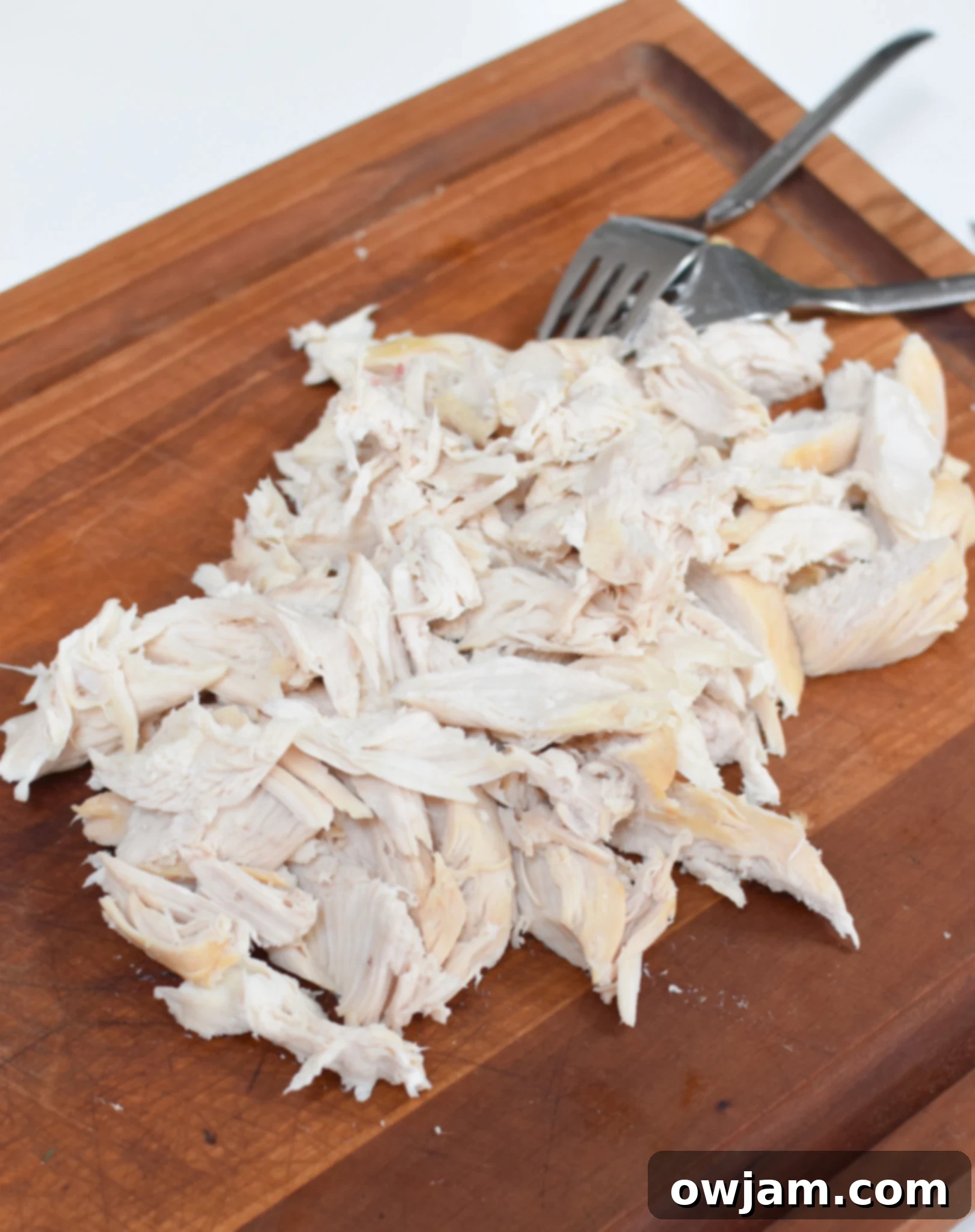 Shredded cooked chicken breast on a wooden cutting board, ready to be mixed into the Lemon Chicken Orzo.