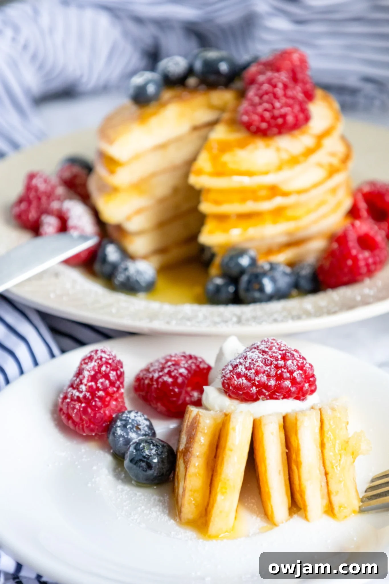 Cloud-Soft Buttermilk Pancakes 4 Close-up of fluffy buttermilk pancakes, some cut into pieces, with a drizzle of syrup and fresh berries.