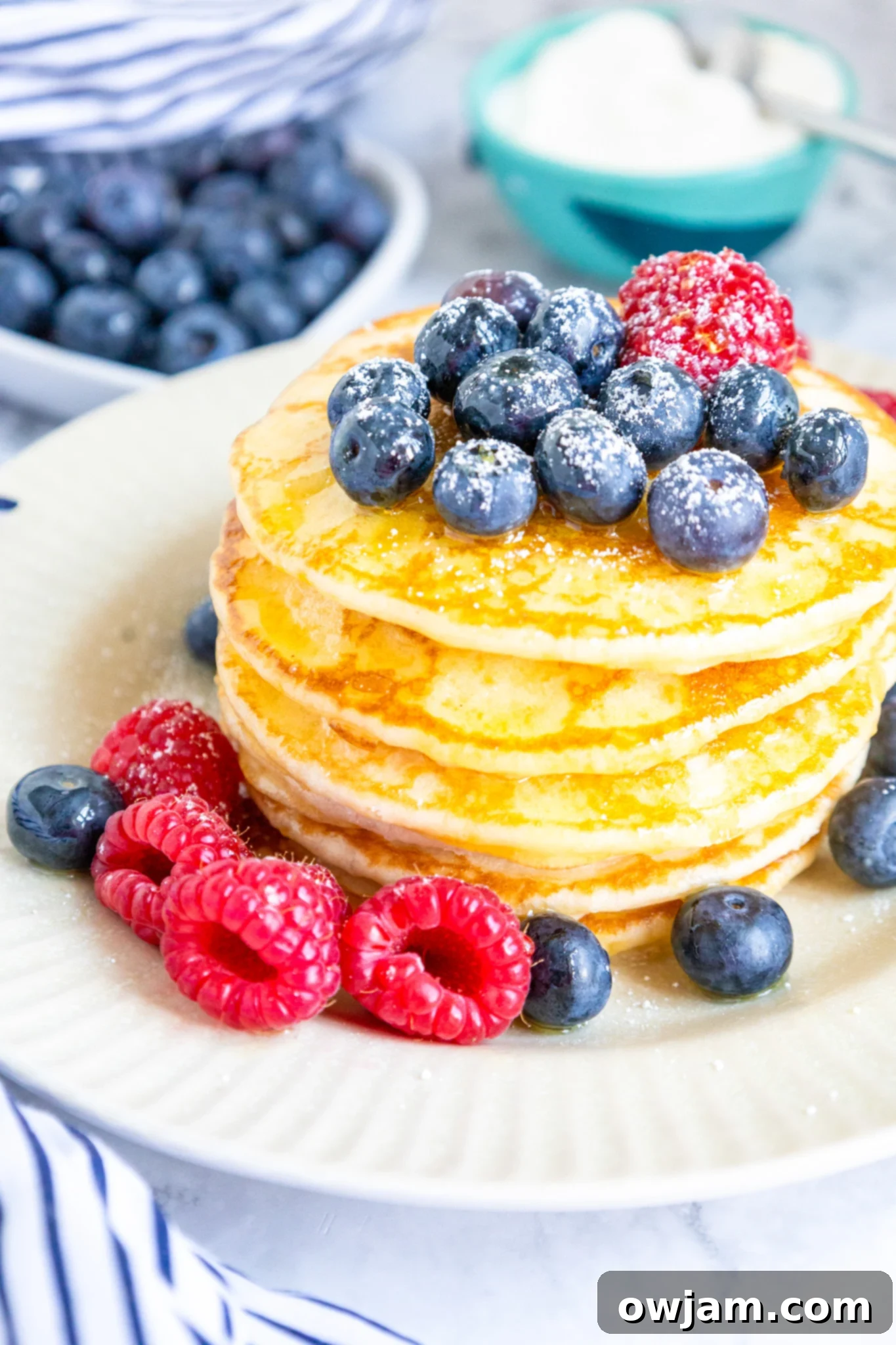 Cloud-Soft Buttermilk Pancakes 5 A stack of golden brown homemade buttermilk pancakes on a white plate, ready to be served.