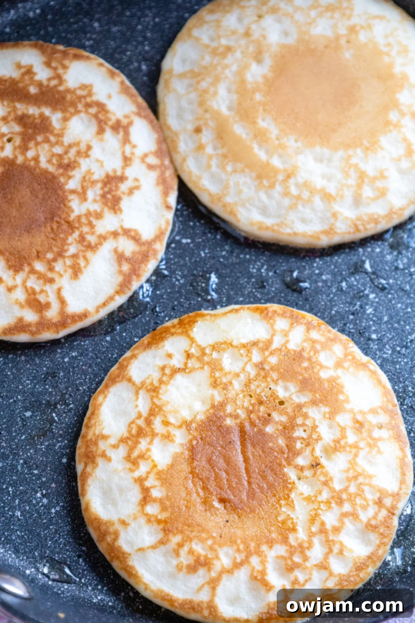 Cloud-Soft Buttermilk Pancakes 6 Homemade buttermilk pancakes cooking on a griddle, showing bubbles forming on the surface.