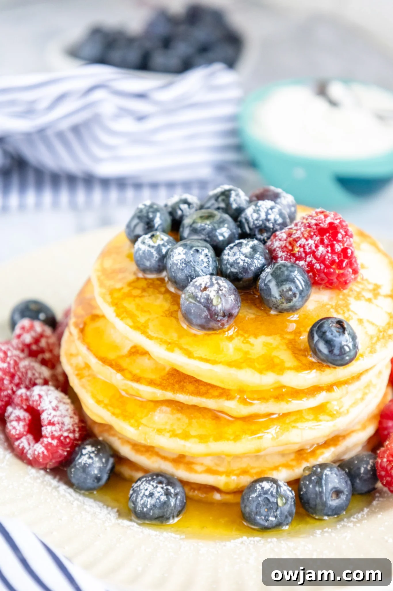 Cloud-Soft Buttermilk Pancakes 7 A stack of homemade buttermilk pancakes dusted with powdered sugar and garnished with fresh raspberries.