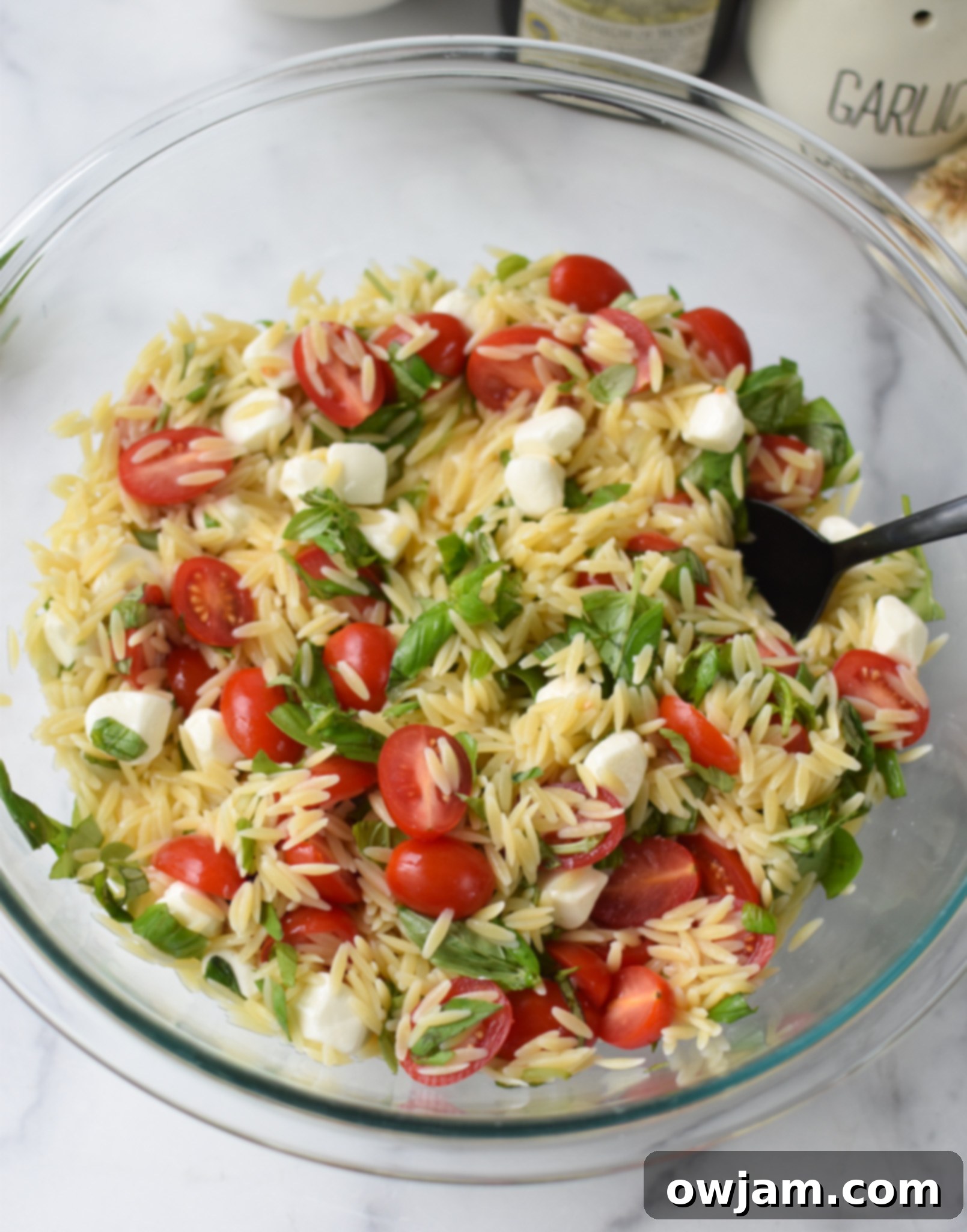 Caprese Orzo Pasta Salad with dressing in glass bowl. 