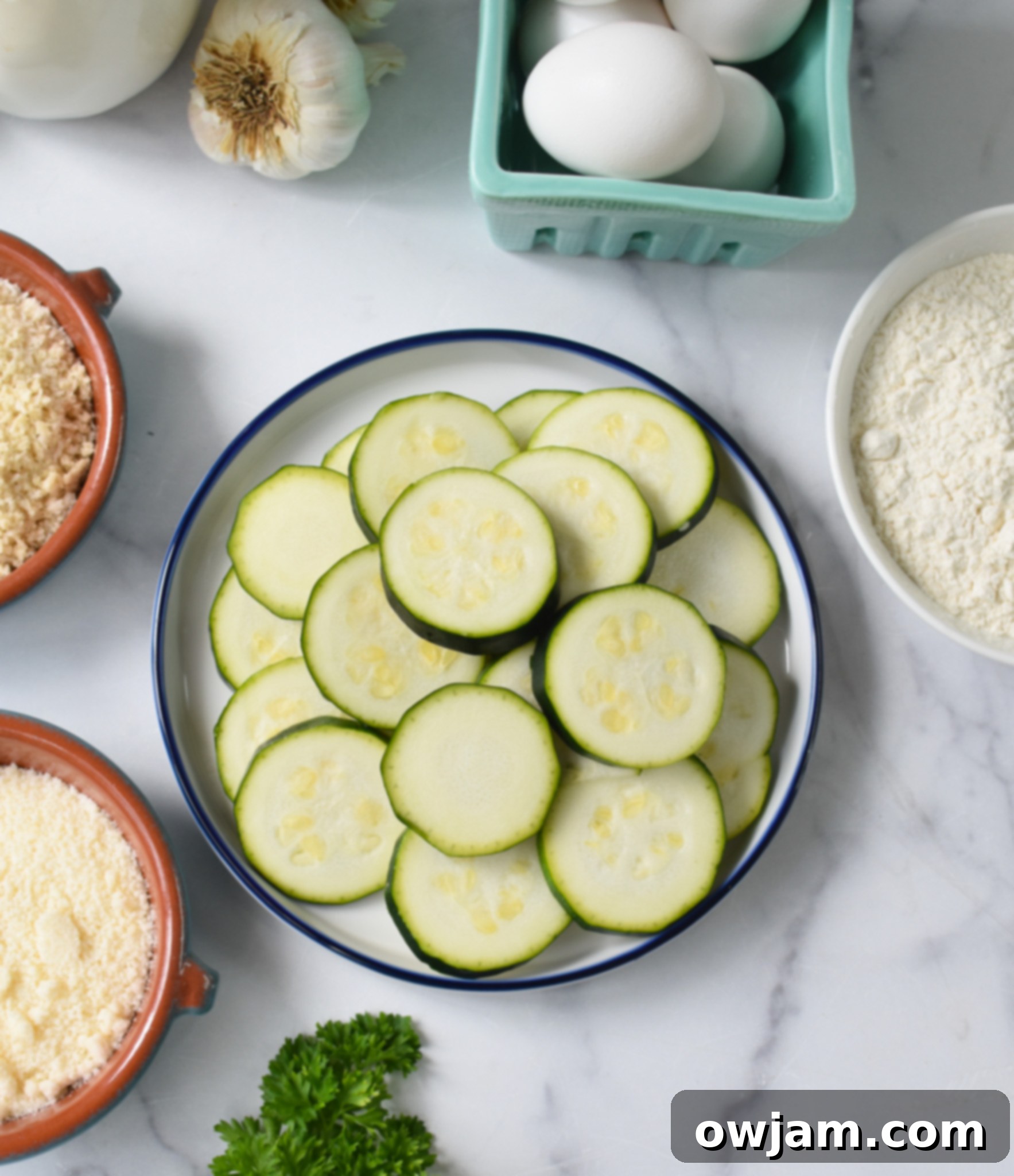 Crispy Air Fryer Zucchini Chips 4 All the fresh ingredients for Air Fryer Zucchini Chips laid out on a cutting board, including zucchini, eggs, flour, breadcrumbs, Parmesan, and spices.