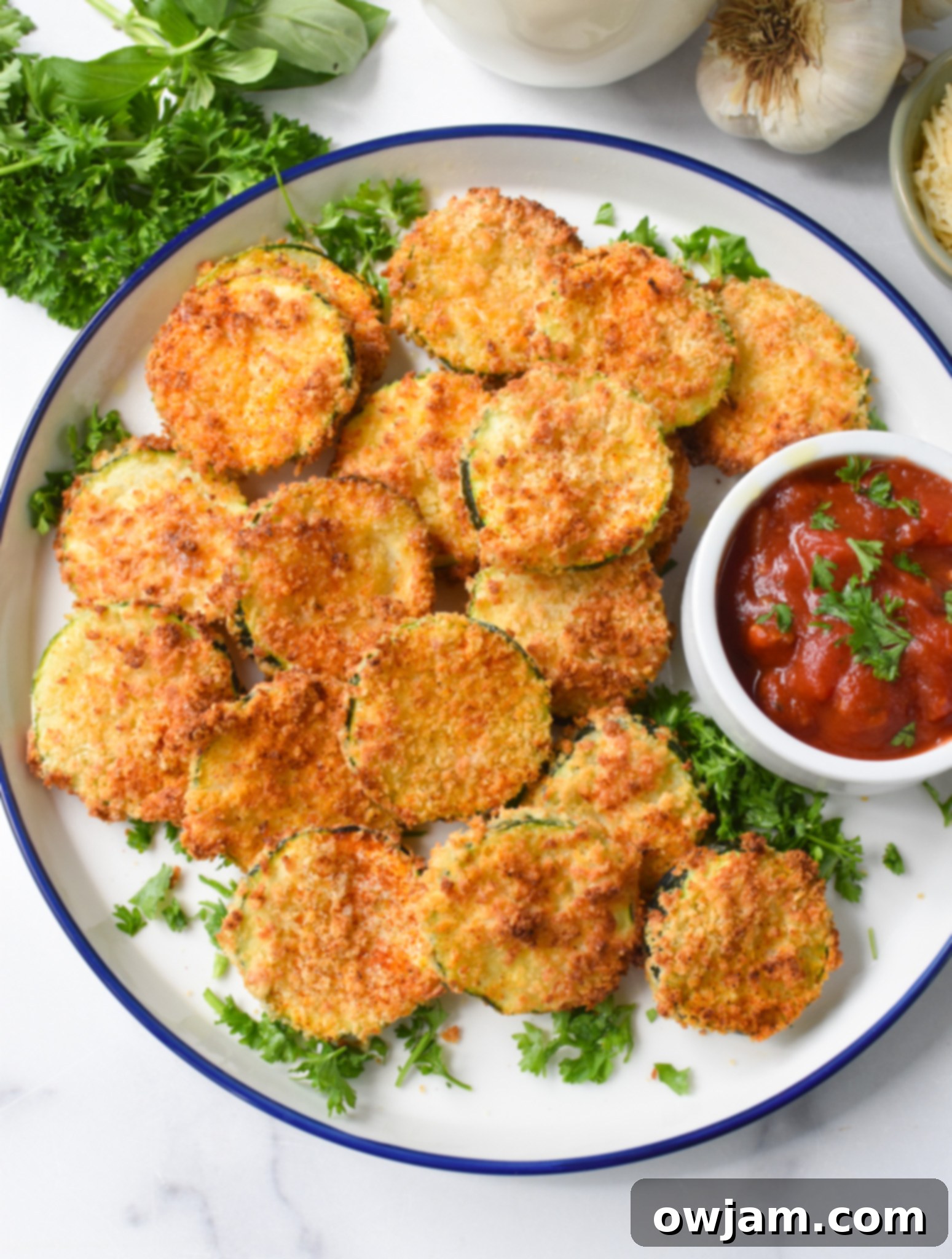 Crispy Air Fryer Zucchini Chips 9 A bowl of crispy Air Fryer Zucchini Chips, garnished with fresh parsley, alongside a bowl of marinara dipping sauce.