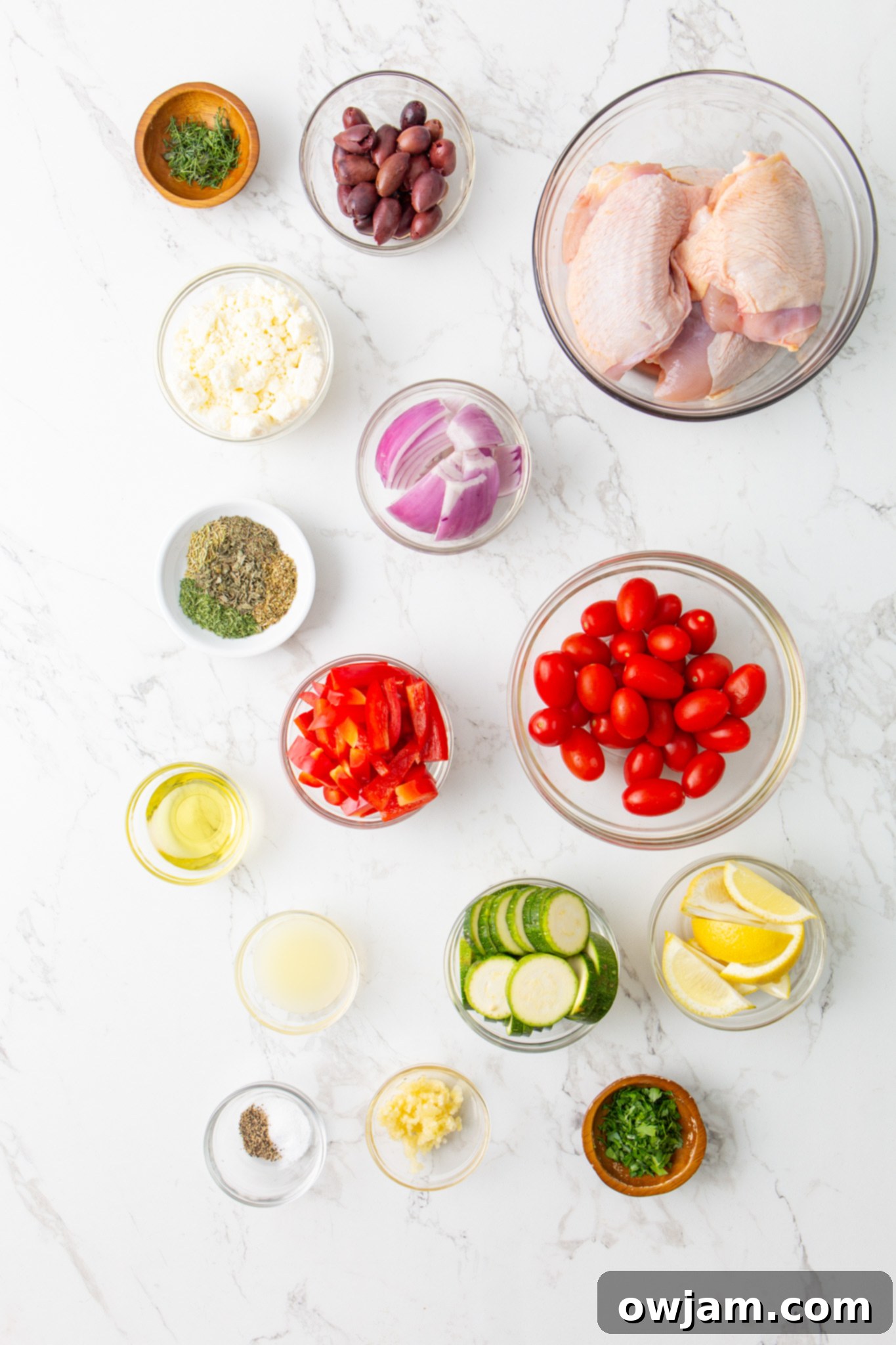 Mediterranean Sheet Pan Chicken 3 Mediterranean Sheet Pan Chicken ingredients laid out on a board, including chicken thighs, various vegetables, olives, and herbs.